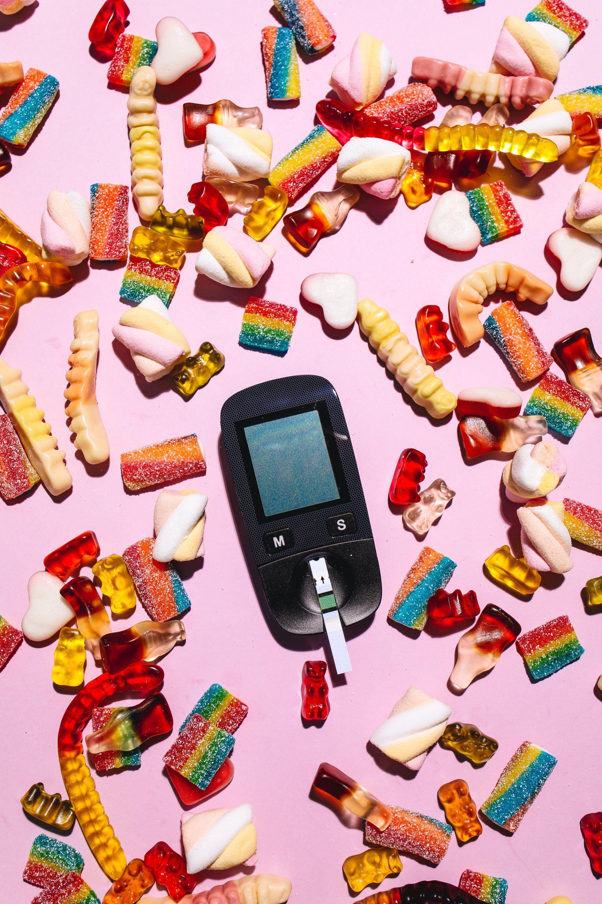 A diabetes monitor is surrounded by candy on a pink background.