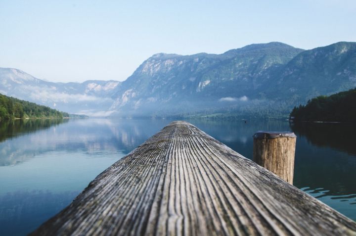 Wooden dock extending into a calm mountain lake with reflections and a clear blue sky