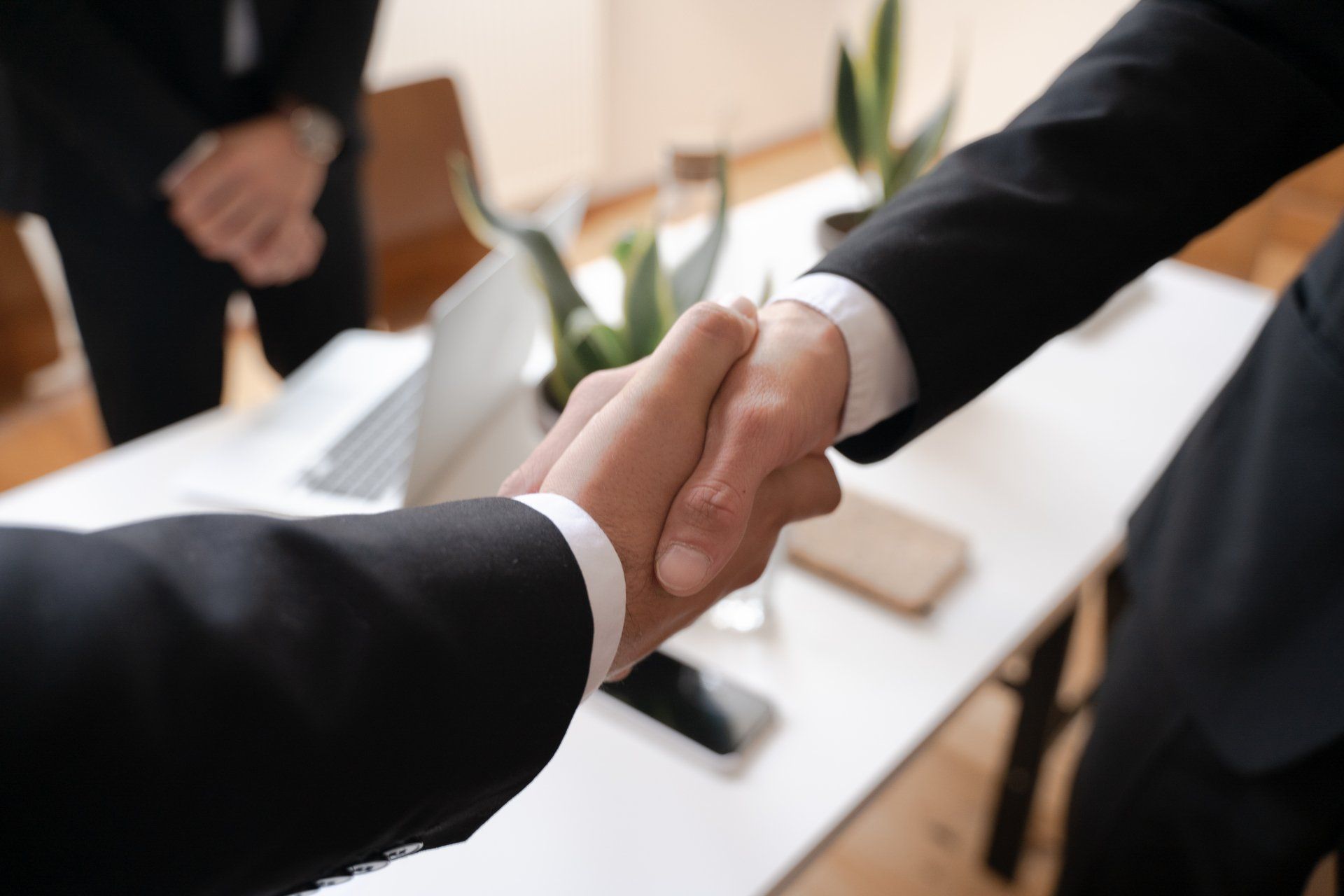 Two men in suits are shaking hands in an office.