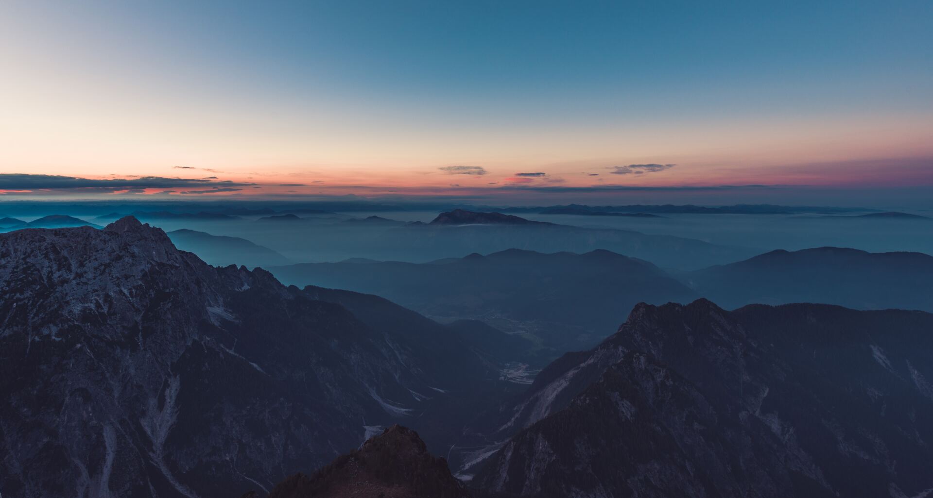 an aerial view of a mountain range at sunset with clouds in the background .