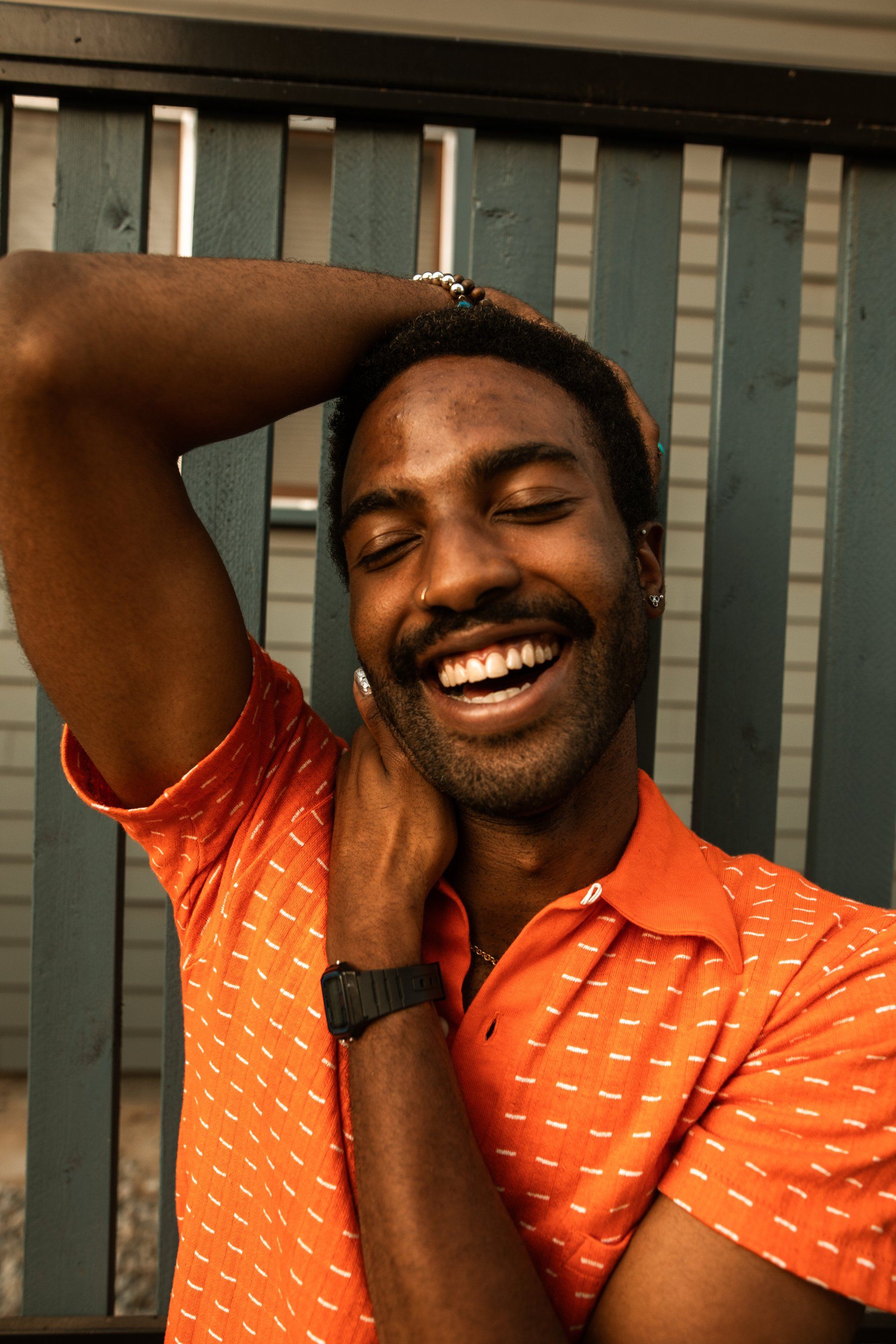 A man wearing an orange shirt and a watch is smiling.