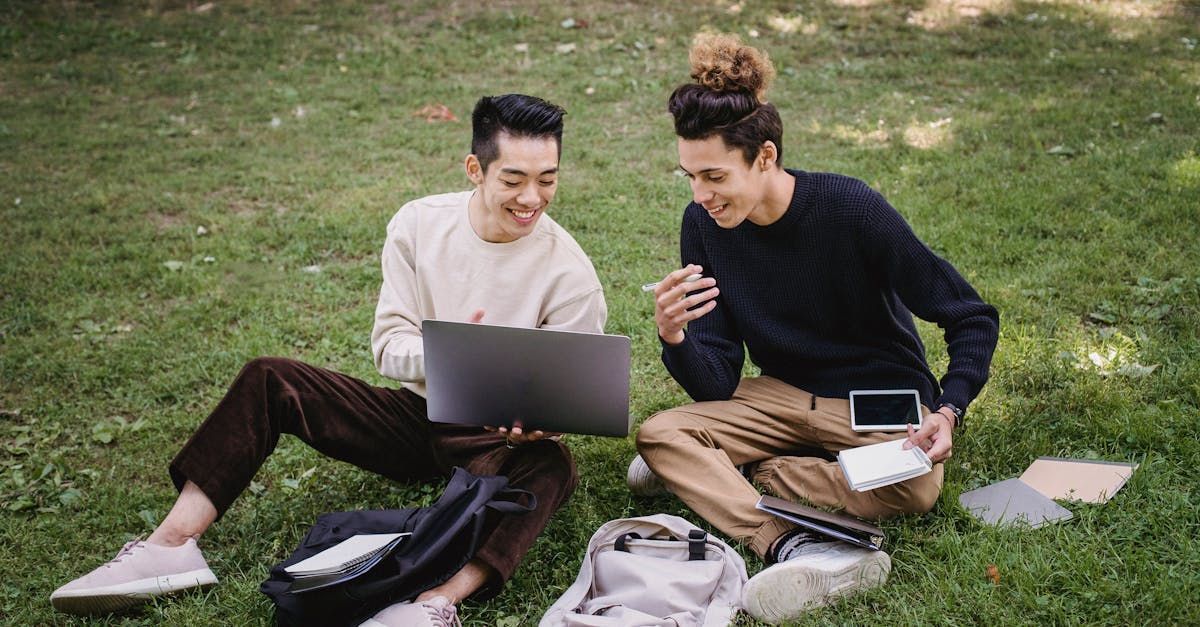 two men are sitting on the grass using laptops.