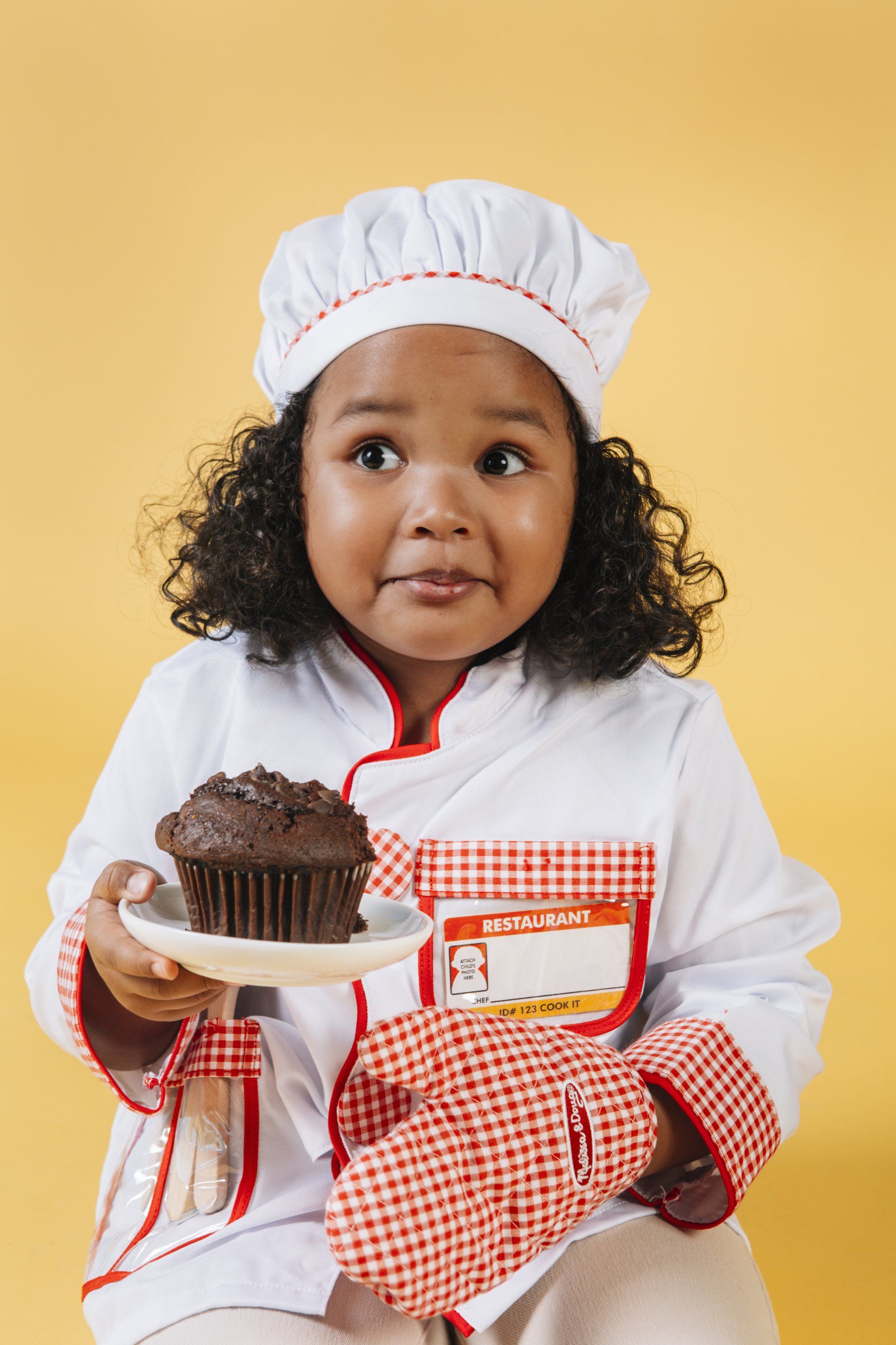 A little girl dressed in chef's whites who is unsure how to give a cake she's just made