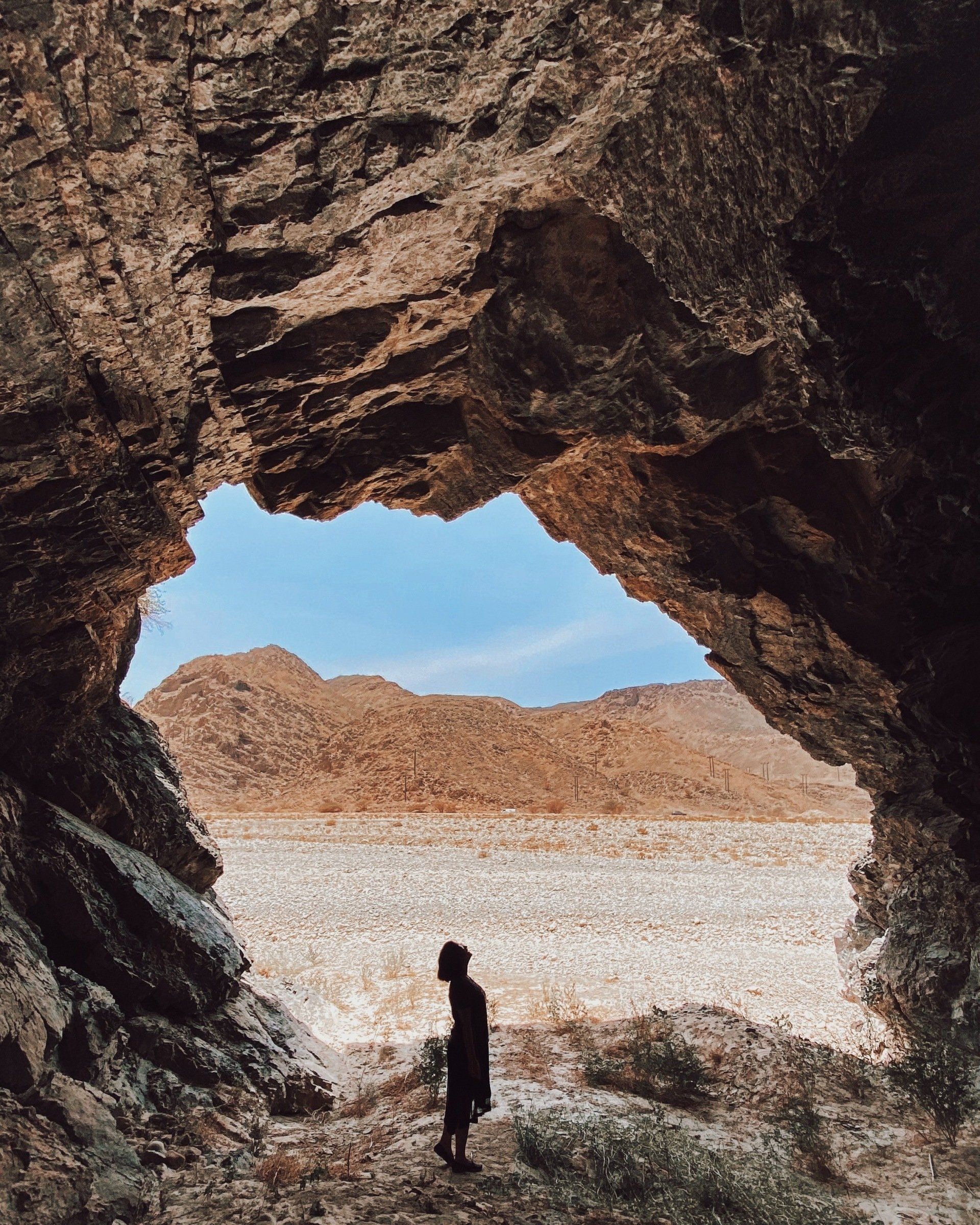 A person is standing in a cave with mountains in the background.