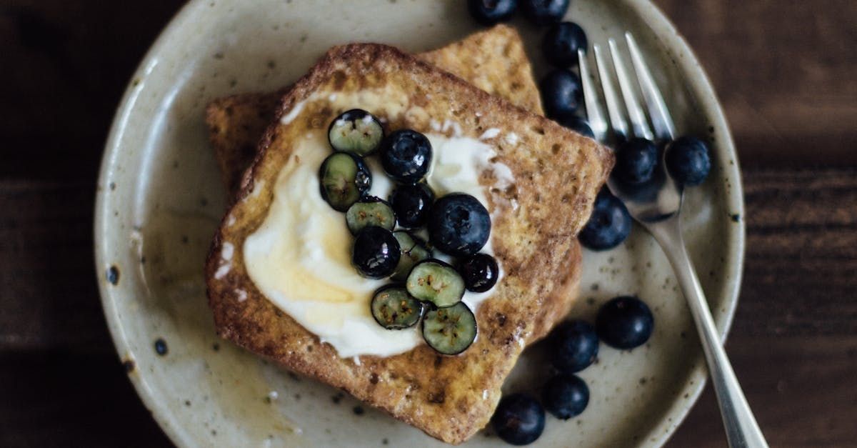 Two slices of french toast with blueberries and whipped cream on a plate with a fork.