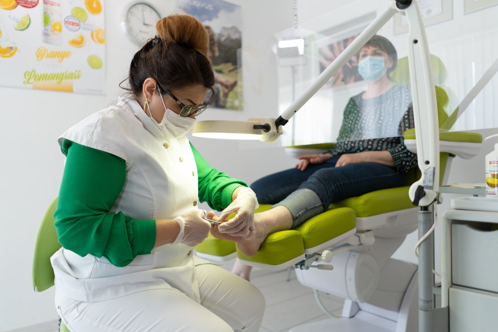 A woman is getting her nails done by a podiatrist while wearing a mask.