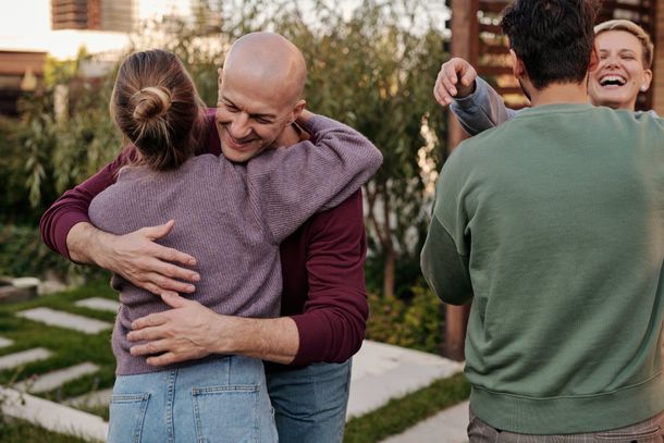 Three people hugging and laughing outdoors in a neighborhood garden at sunset