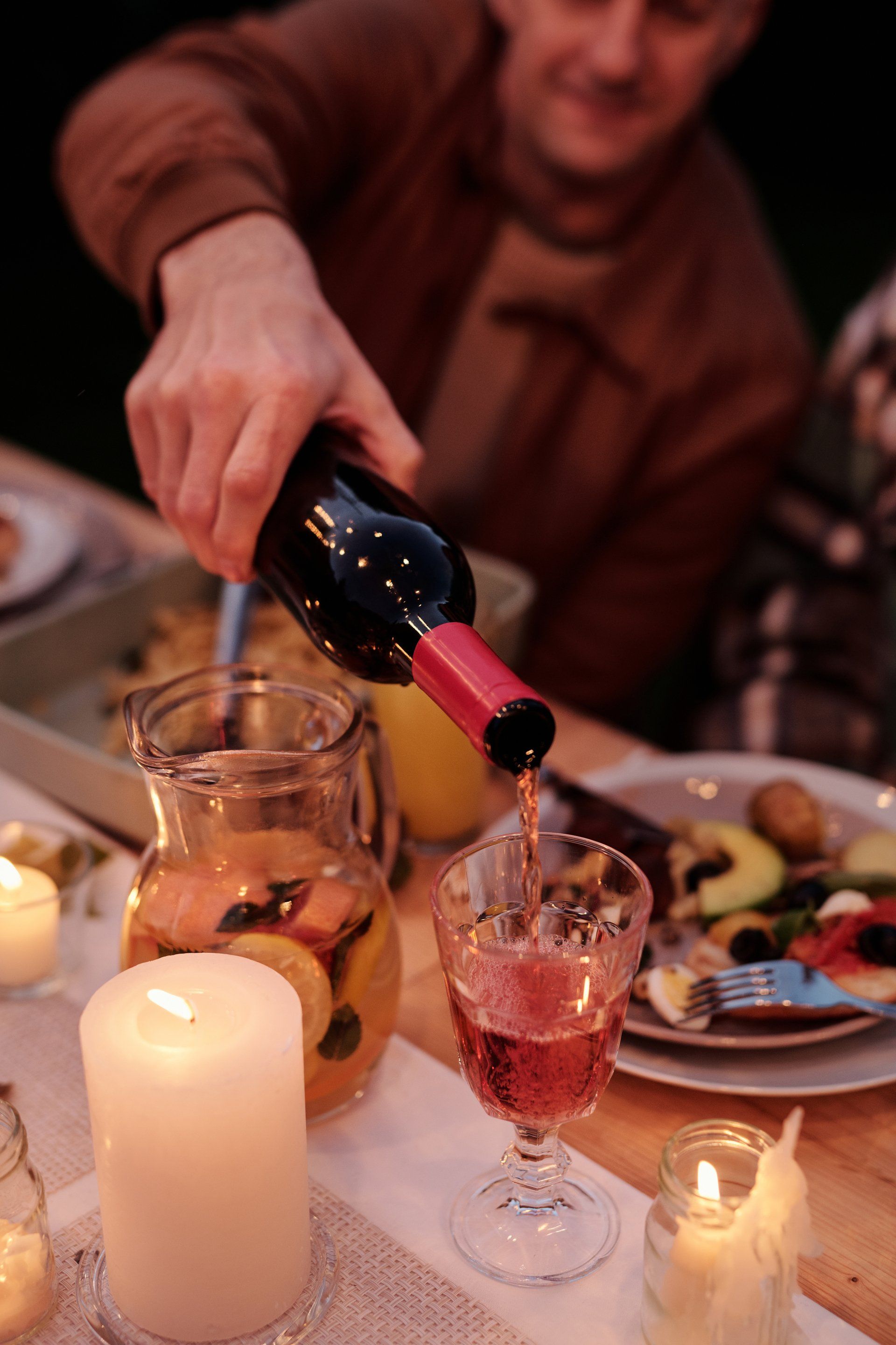 A man is pouring wine into a glass at a dinner table.