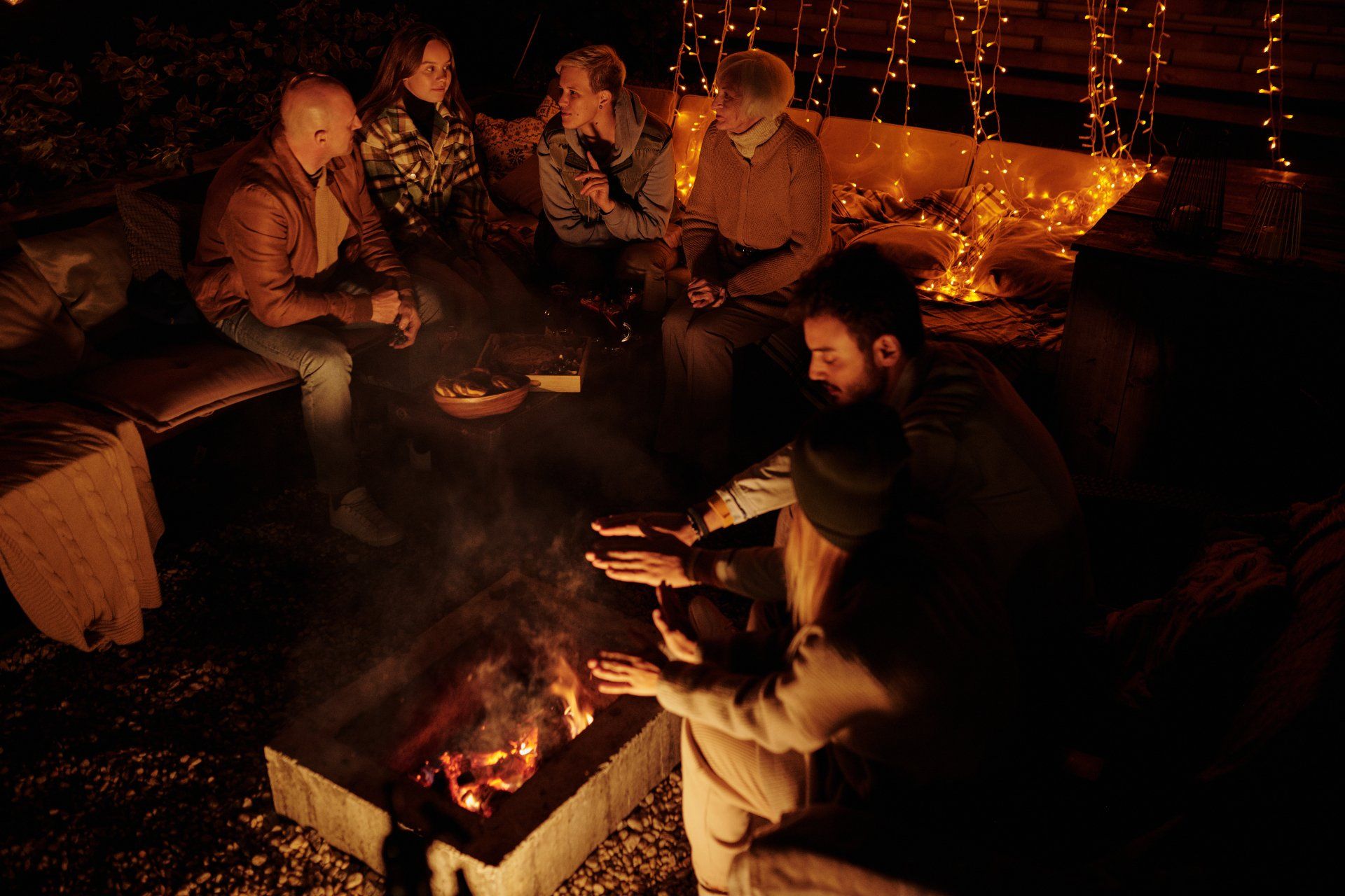 A group of people are sitting around a fire pit at night.