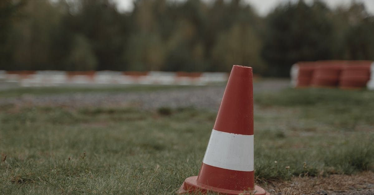 A red and white traffic cone is sitting on the grass.