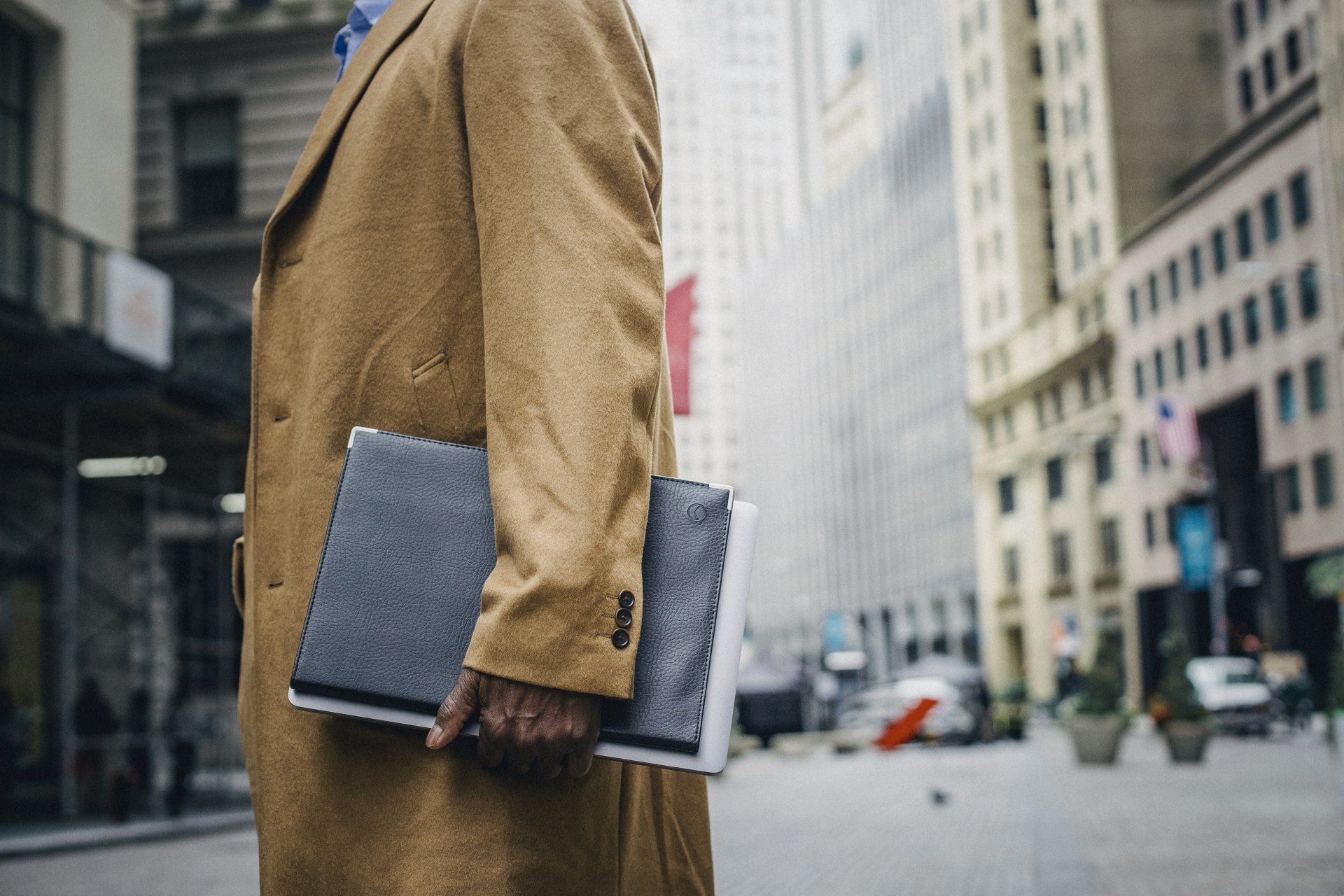 Person in tan coat holds two notebooks on city street.