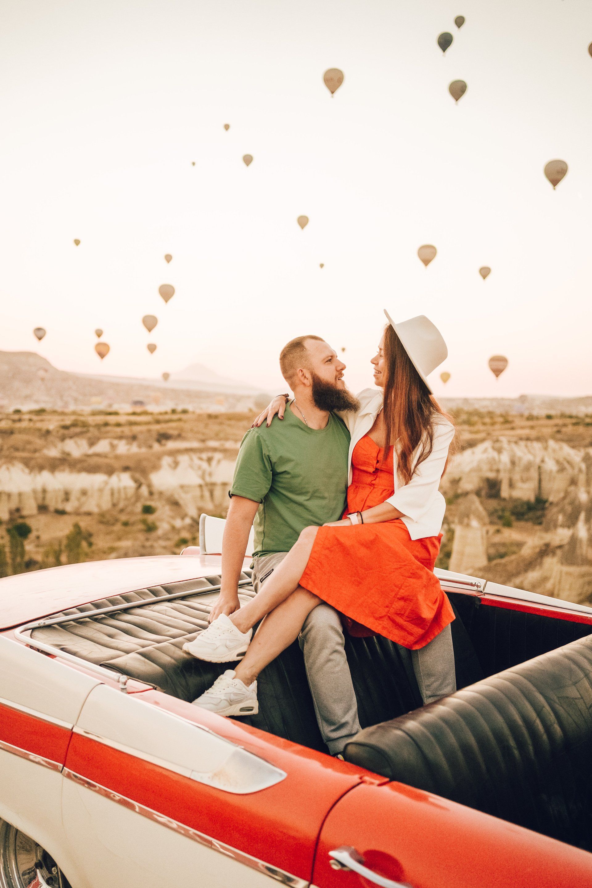 A man and a woman are sitting on the back of a red car.
