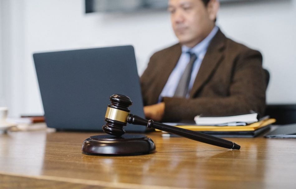 A judge is sitting at a desk with a laptop and a gavel.