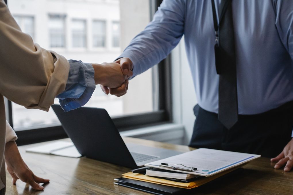 A man and a woman are shaking hands in front of a laptop.