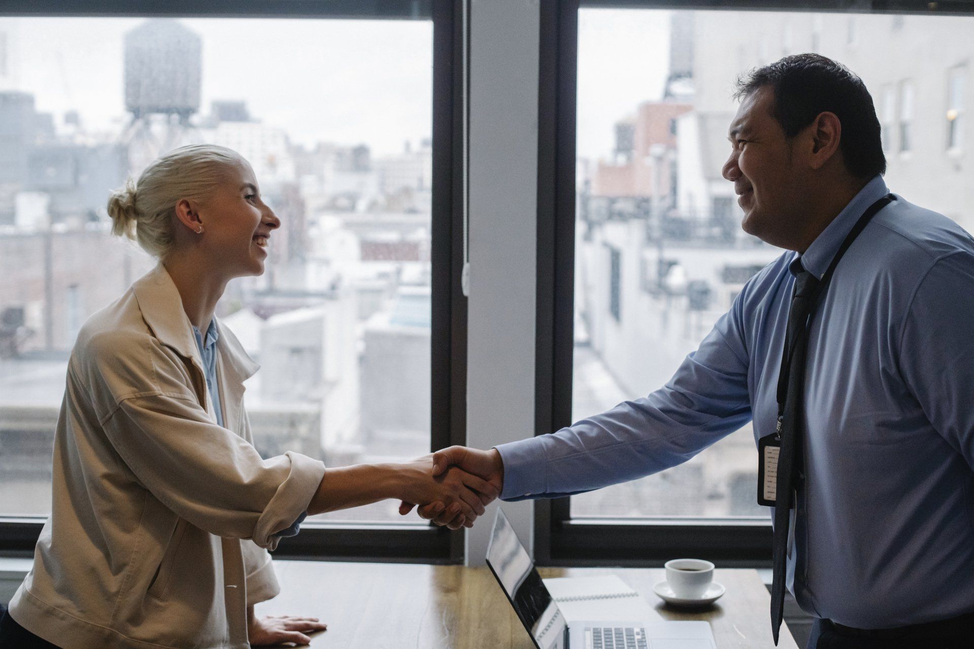 A man and a woman are shaking hands in front of a window.