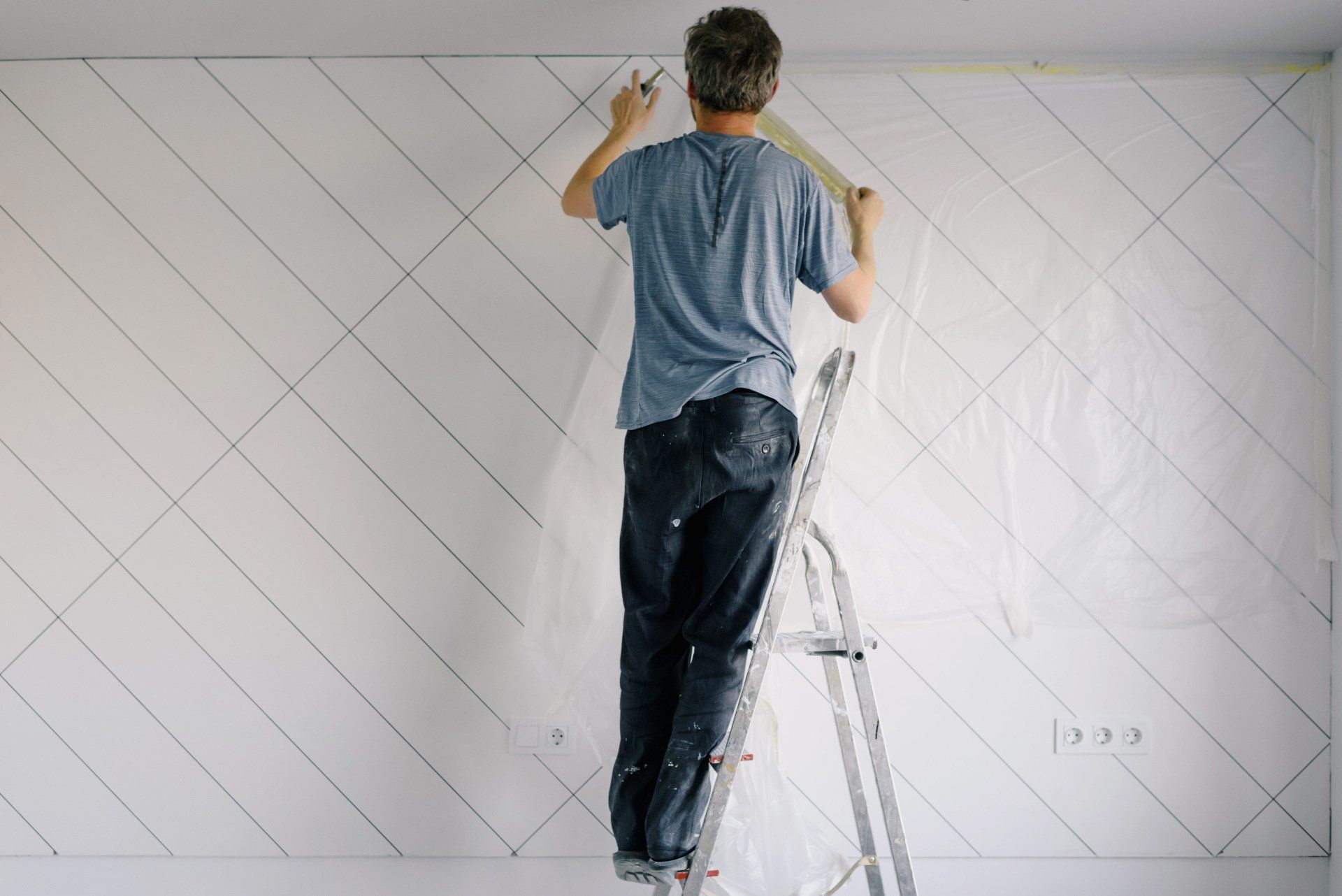 An experienced painter meticulously applies tape on a wall, preparing for a geometric paint design.