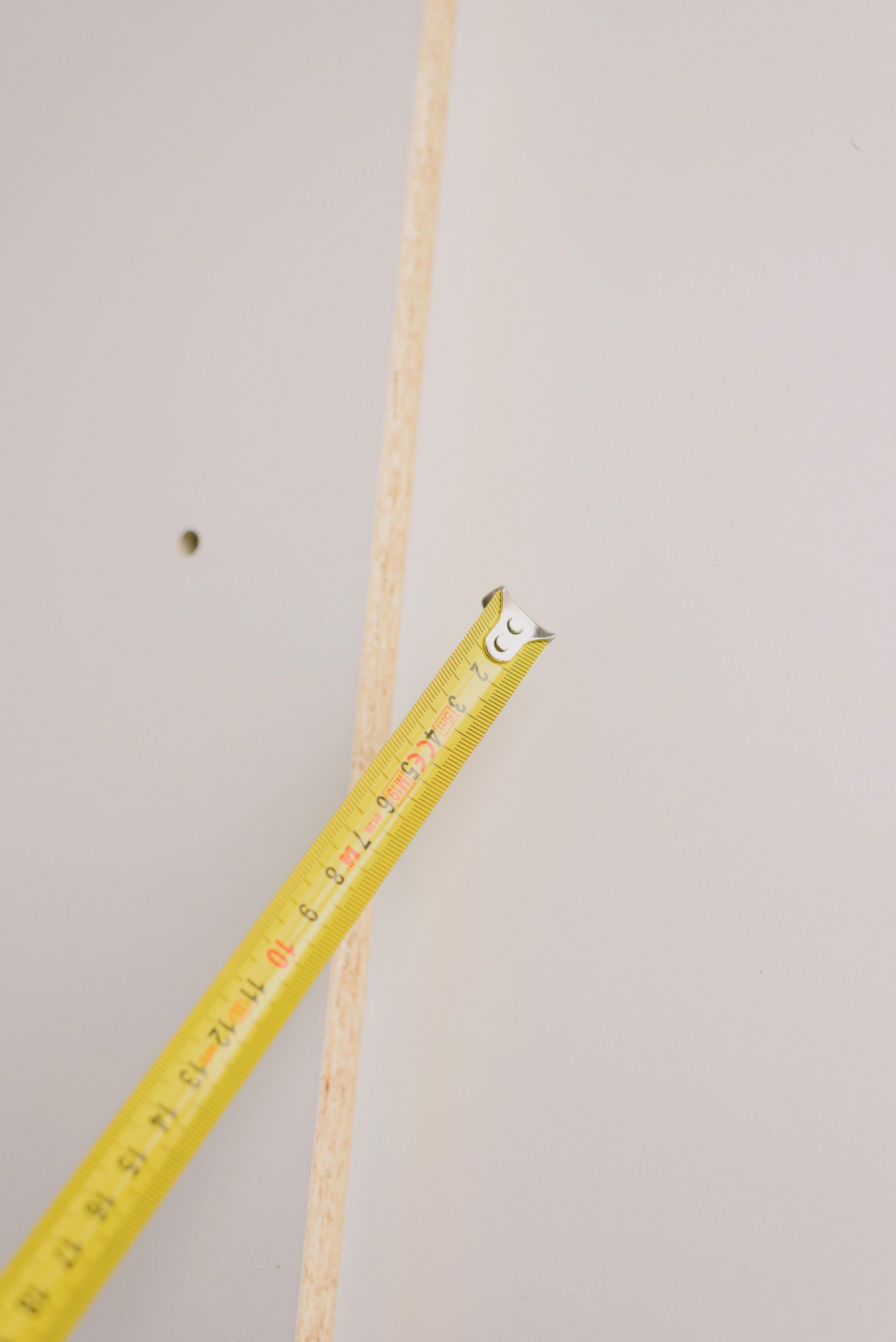 A yellow tape measure is sitting on a white wall.