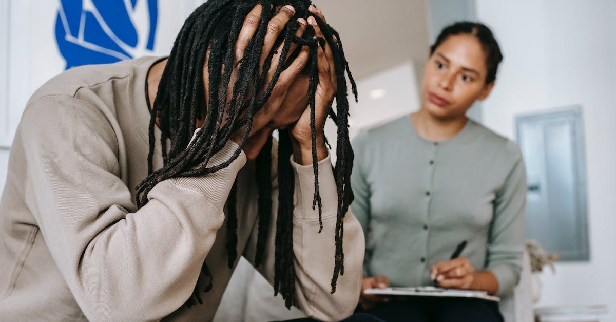 A man with dreadlocks is sitting in front of a woman holding a clipboard.