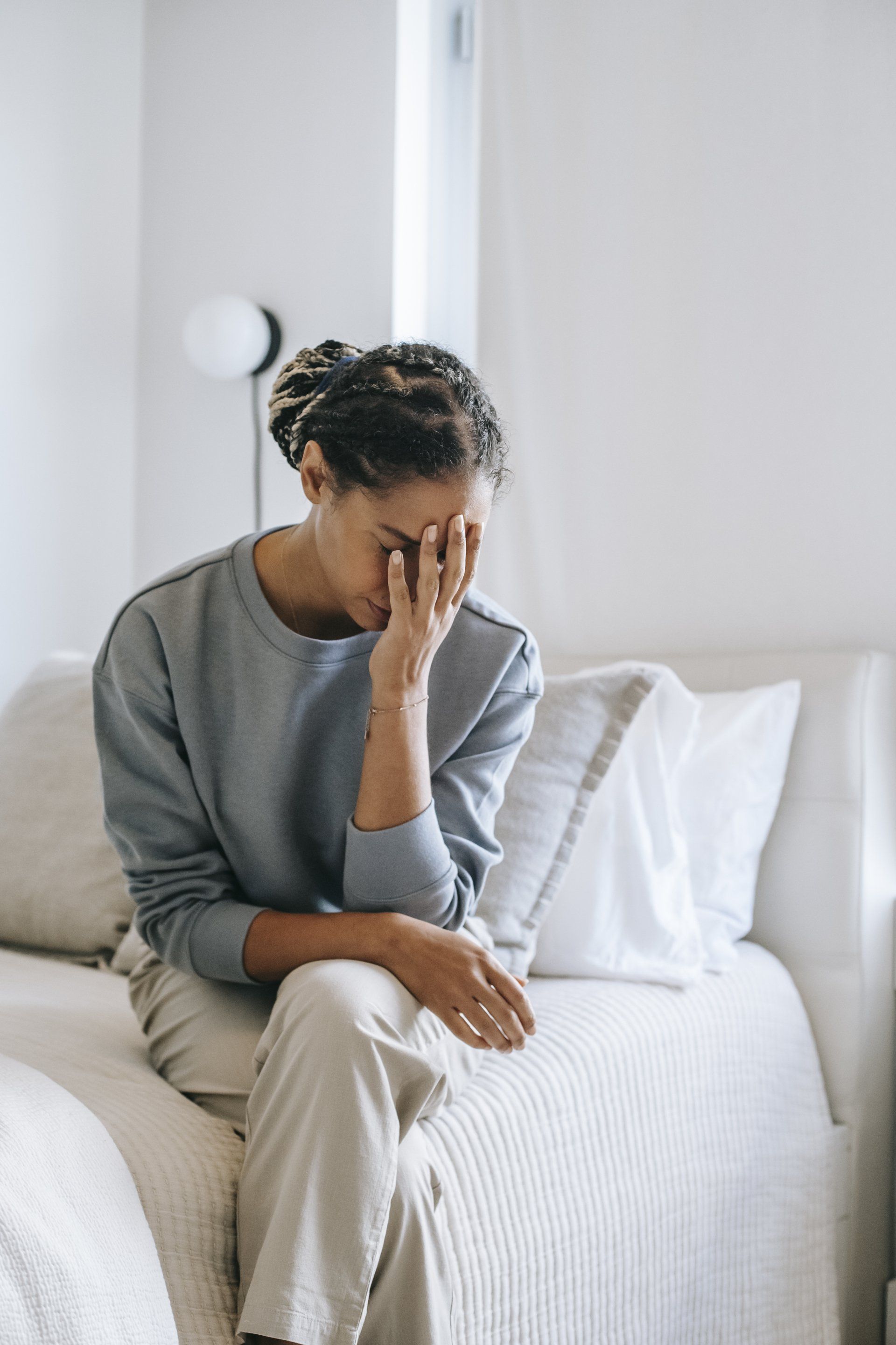 A woman is sitting on a couch with her head in her hands.