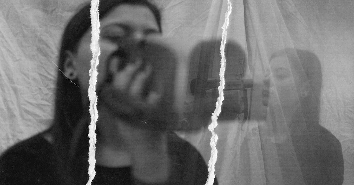 A black and white photo of a woman taking a selfie behind a curtain.