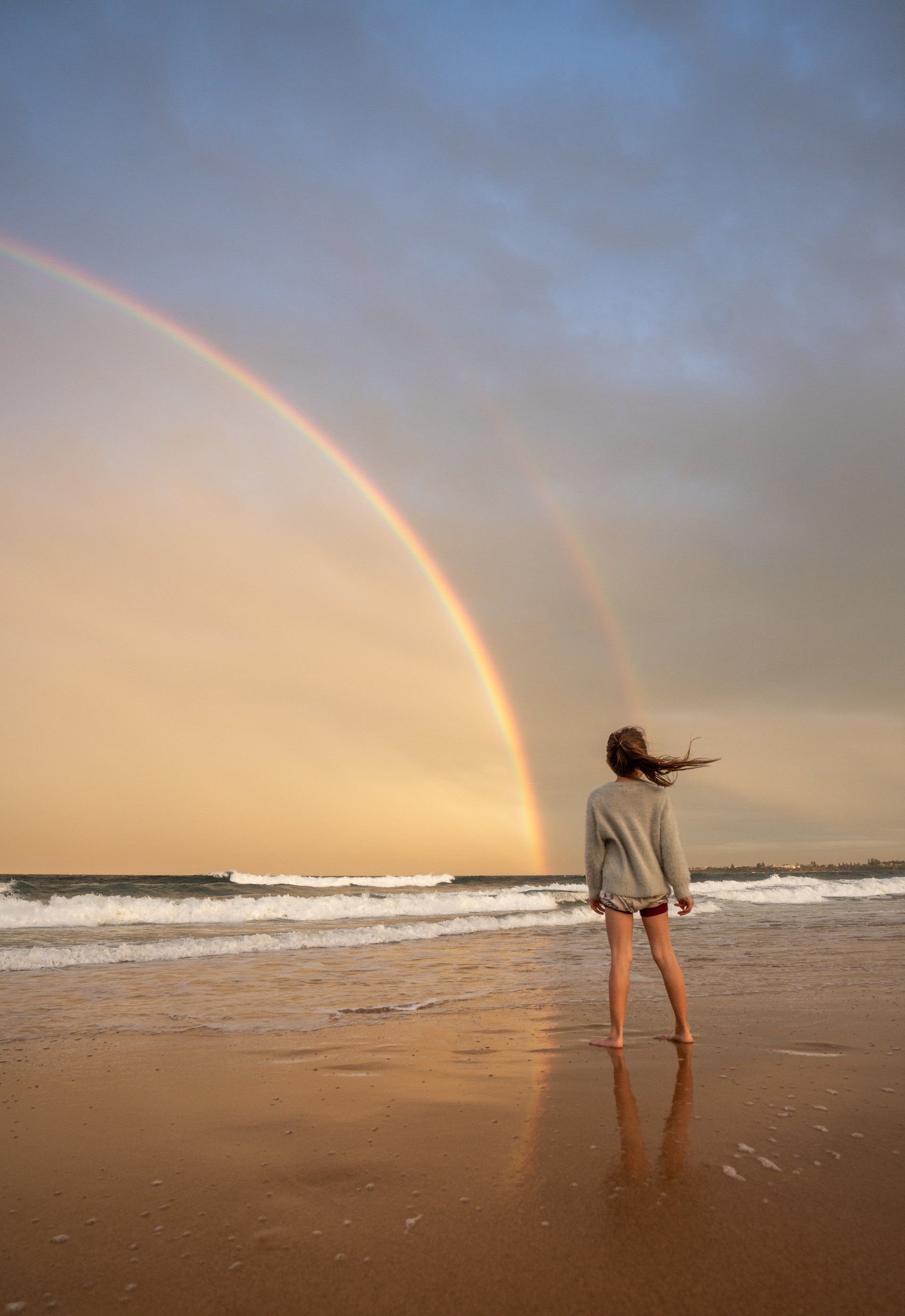 woman stood on the beach under a rainbow