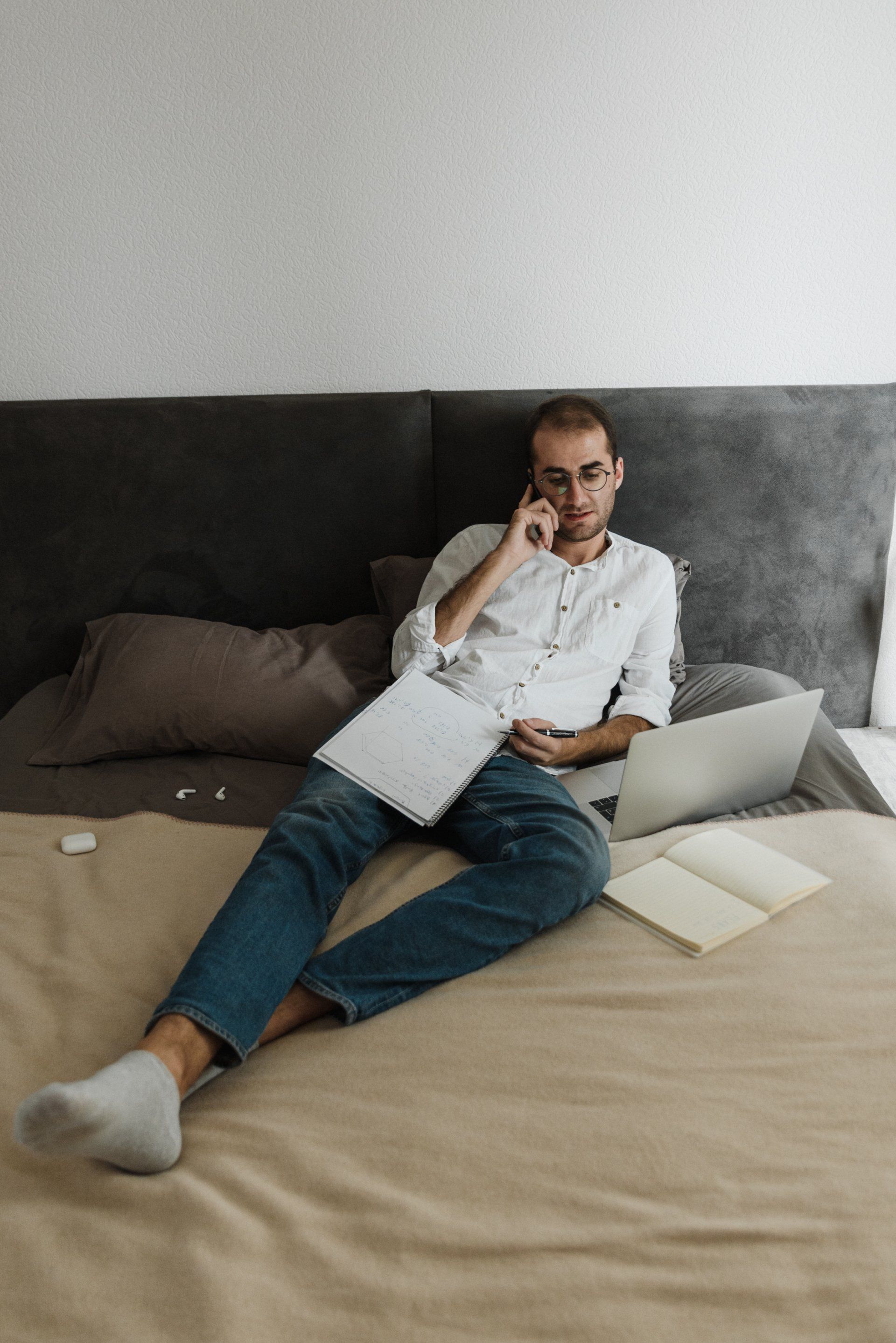 Man lounging on bed with papers and laptop around him