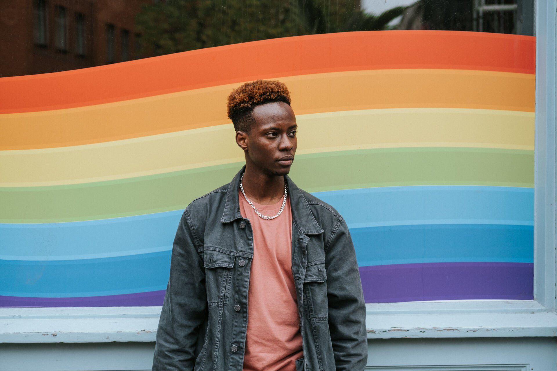 A man is standing in front of a rainbow flag.