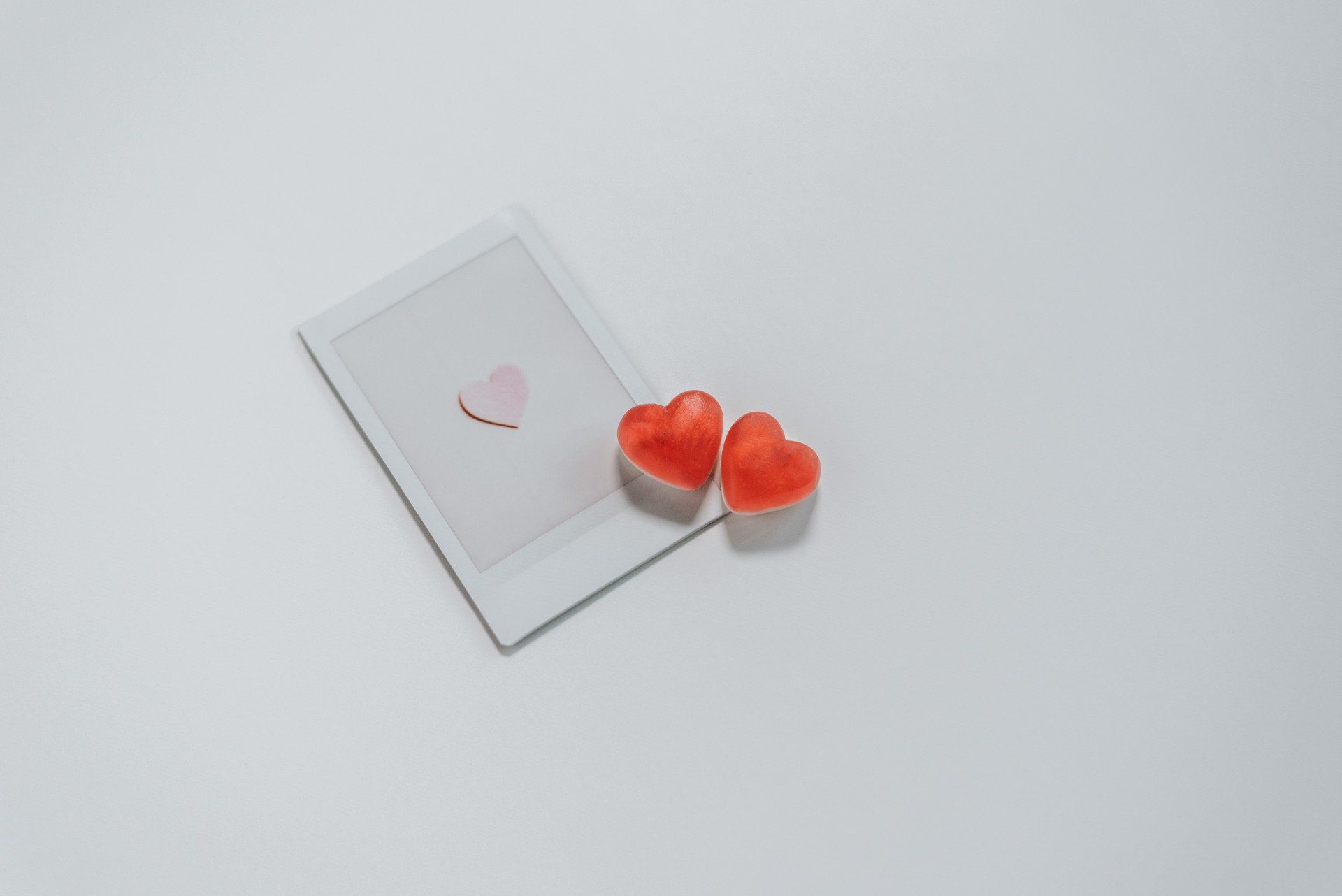 Two red hearts are sitting next to a polaroid picture on a white surface.