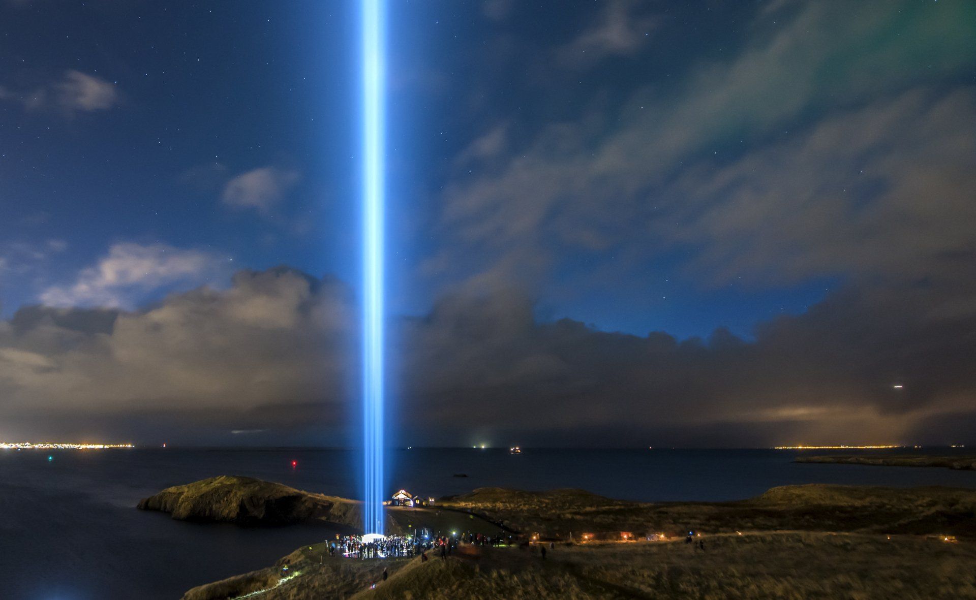 A tall light tower is shining over the ocean at night.