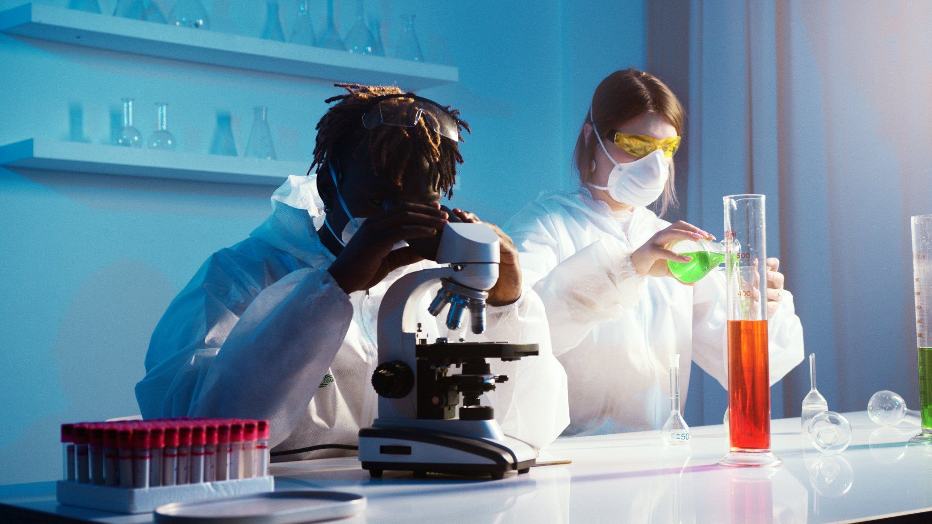 A man and a woman are looking through a microscope in a laboratory.