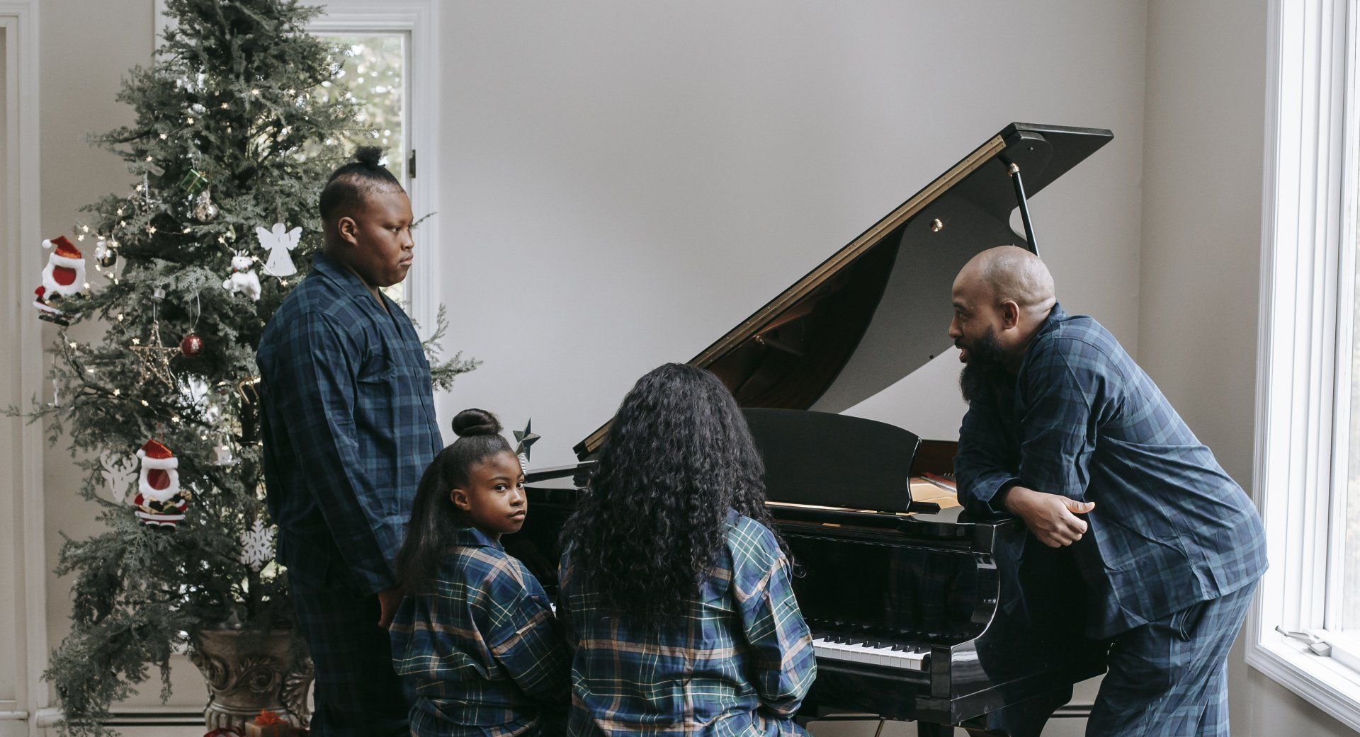 A family is standing around a piano in front of a christmas tree.