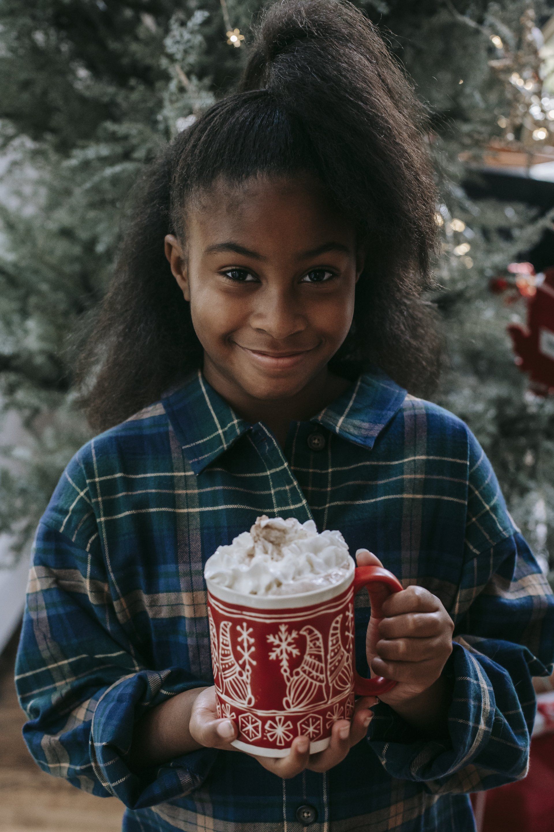 a little girl is holding a mug of hot chocolate with whipped cream