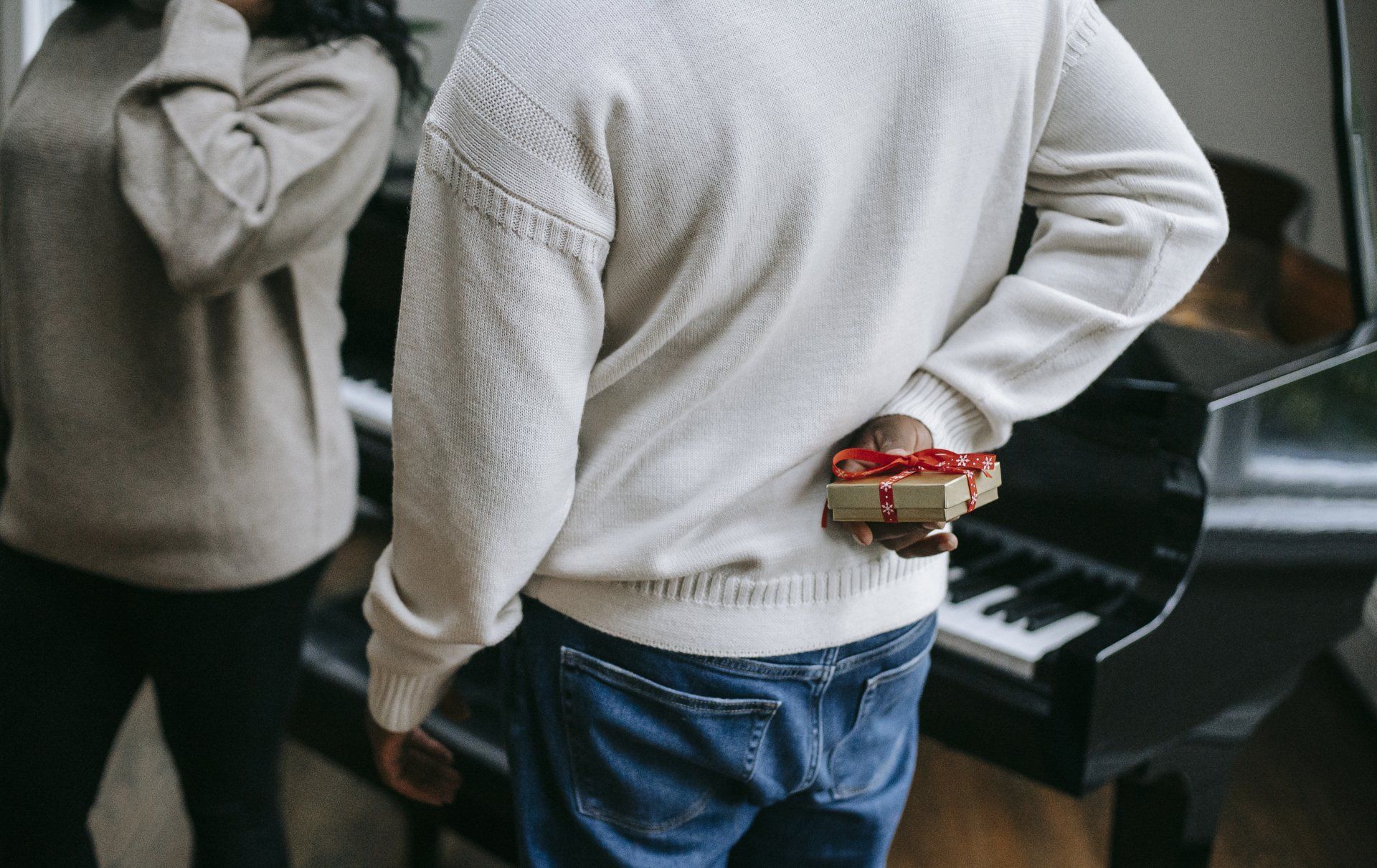 a man is holding a gift box behind his back in front of a piano .