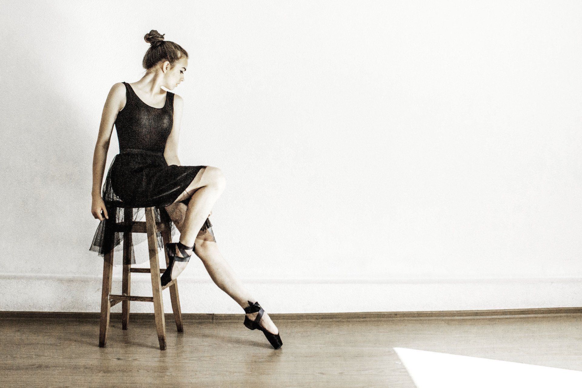 A woman in a black dress is sitting on a stool with her legs crossed.