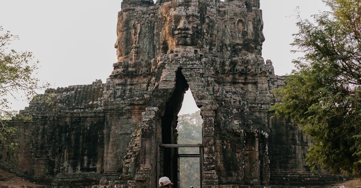 A man is standing in front of a large stone building with a face carved into it.