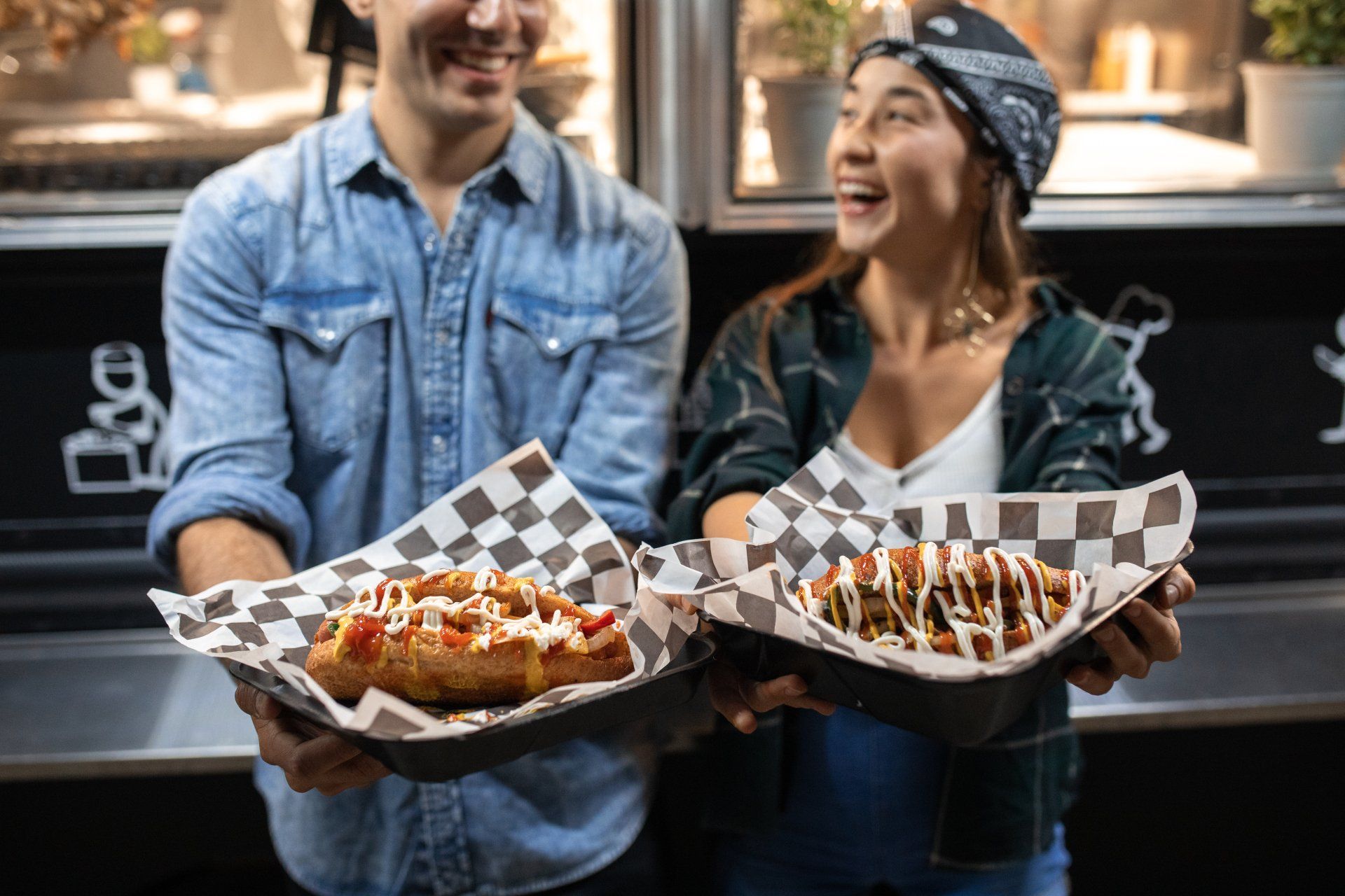 A man and a woman are holding plates of food in front of a food truck.