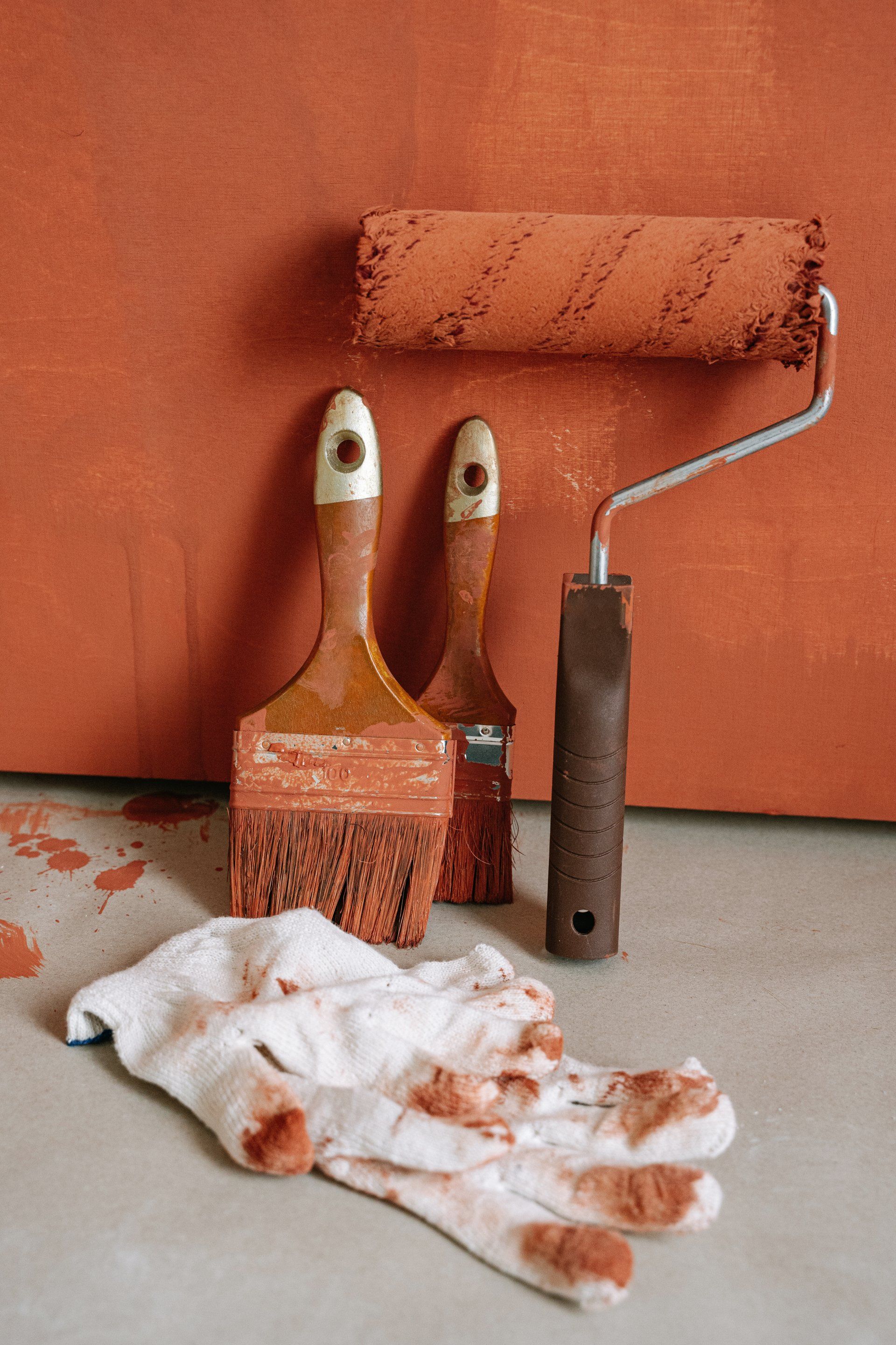 a paint roller , brushes , and gloves are sitting on the floor .