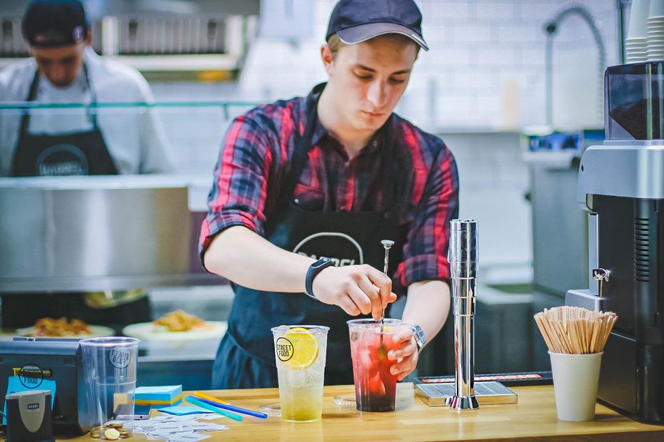 A man in an apron is preparing a drink in a kitchen.