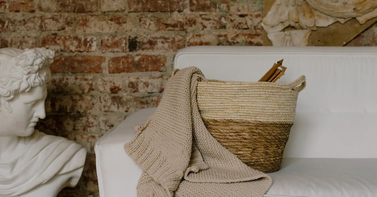 A basket with pencils in it is sitting on a couch next to a statue.