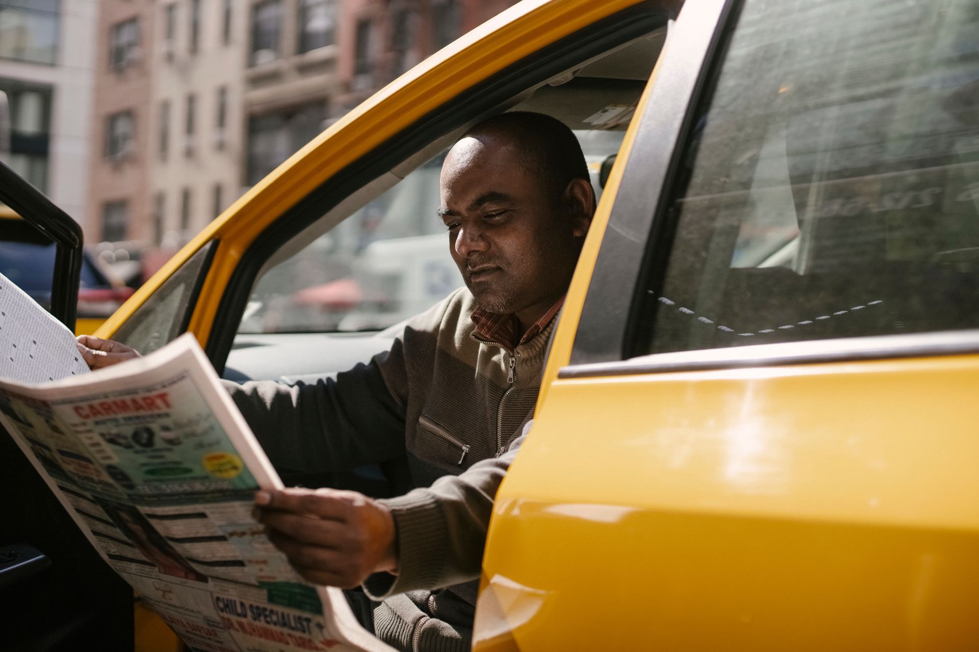 A man is sitting in a taxi reading a newspaper