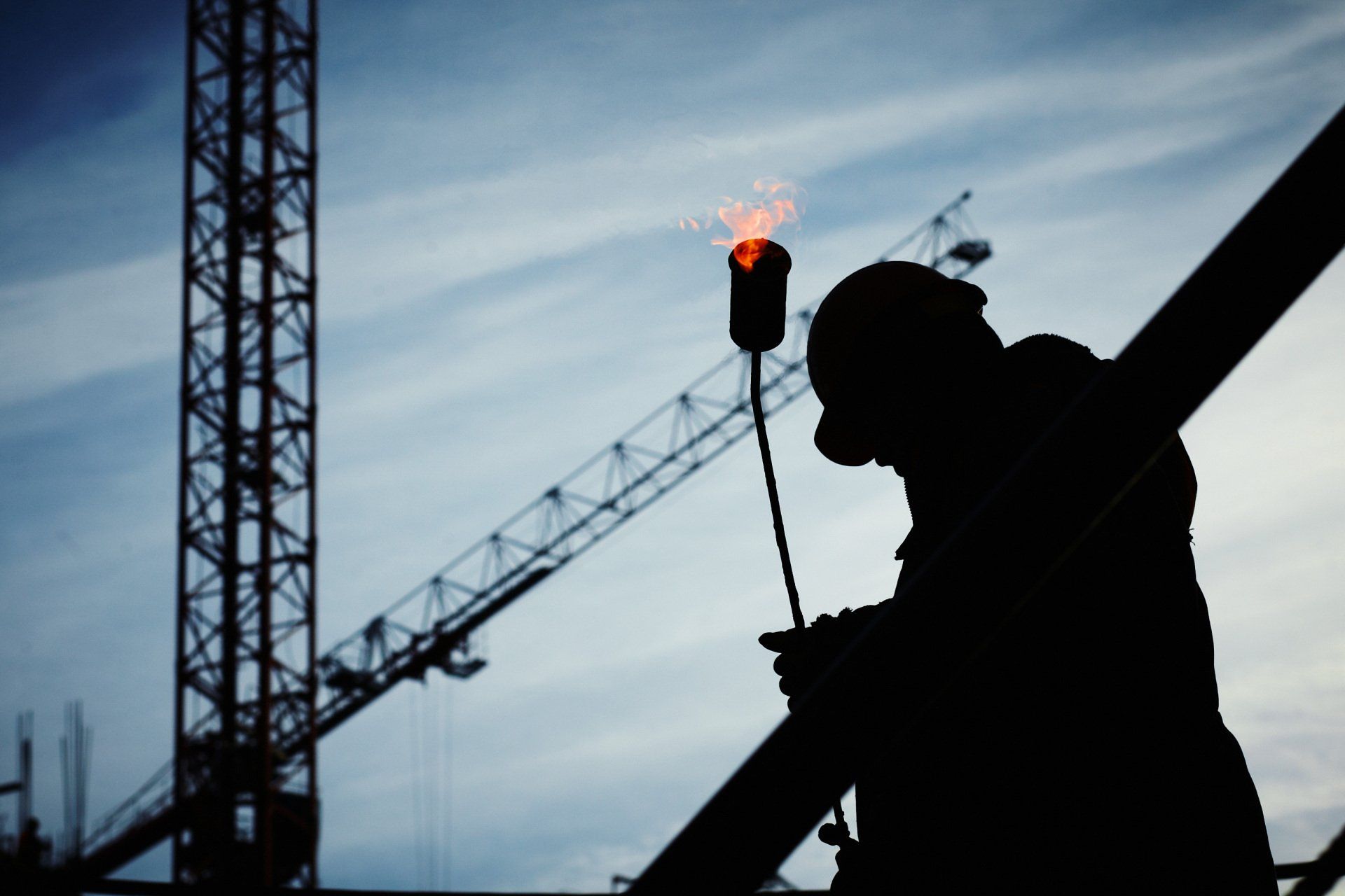 a silhouette of a man holding a torch with a crane in the background