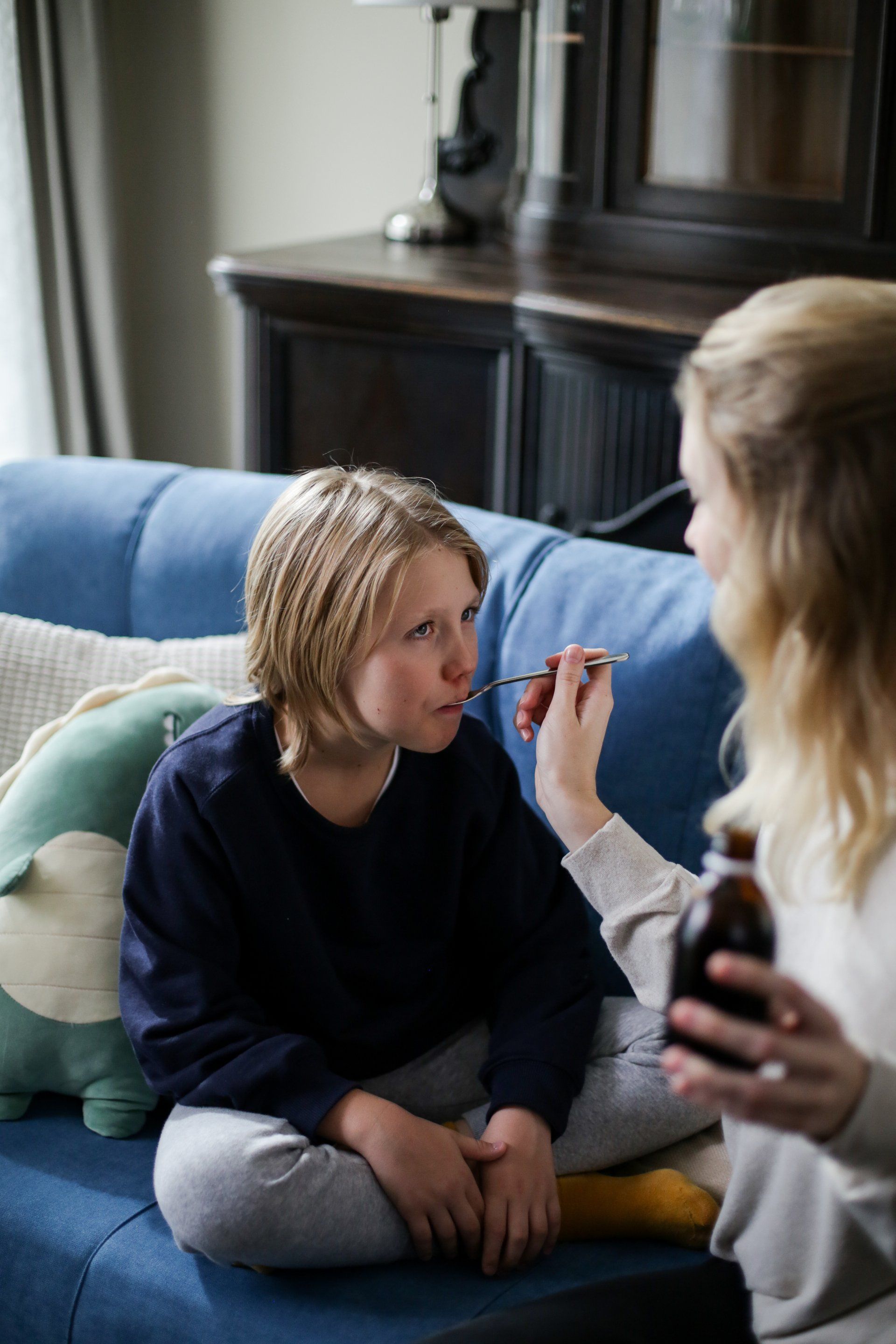 A woman is giving a child a syrup while sitting on a couch.