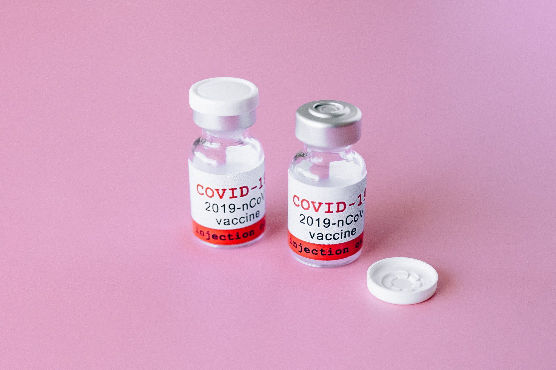 Two bottles of covid-19 vaccine on a pink background.