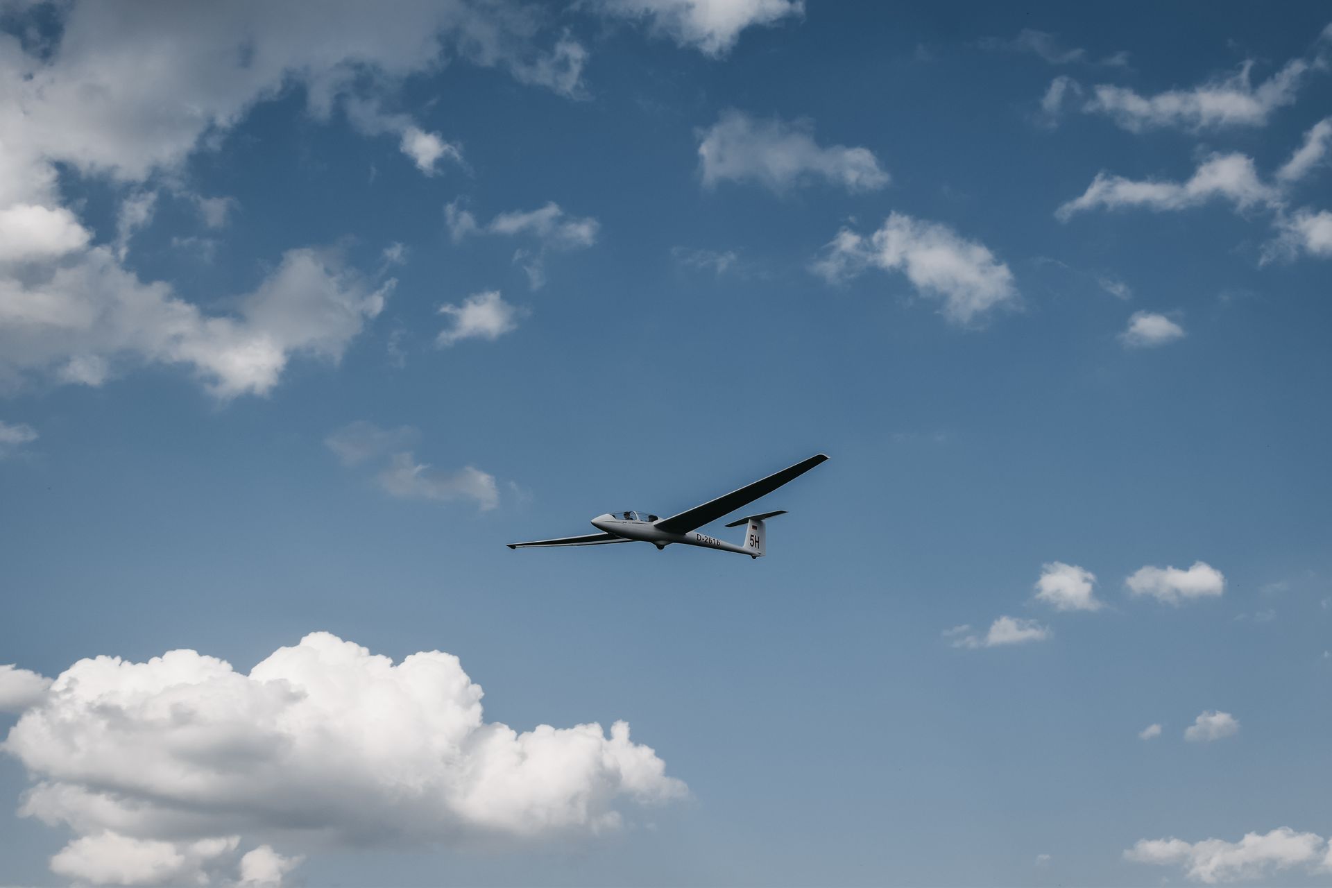 A glider plane is flying through a cloudy blue sky.