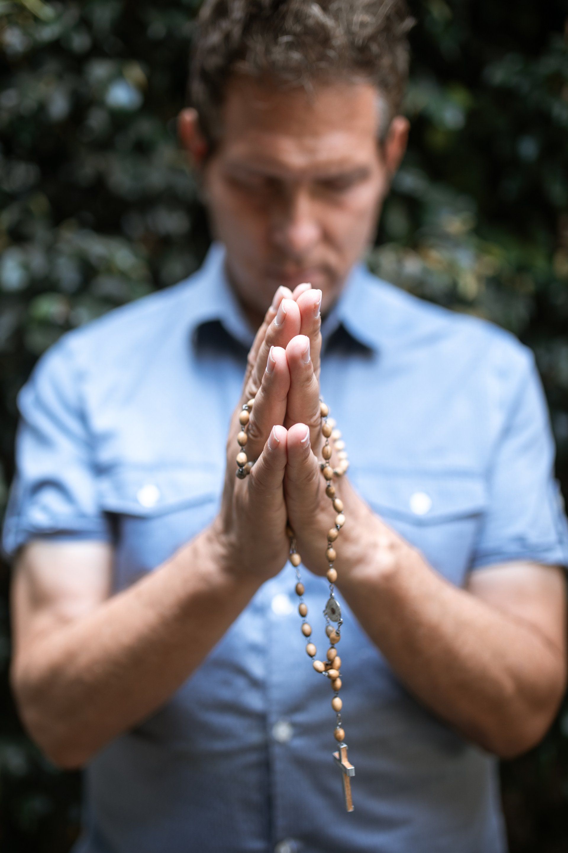 A man is praying with a rosary in his hands.
