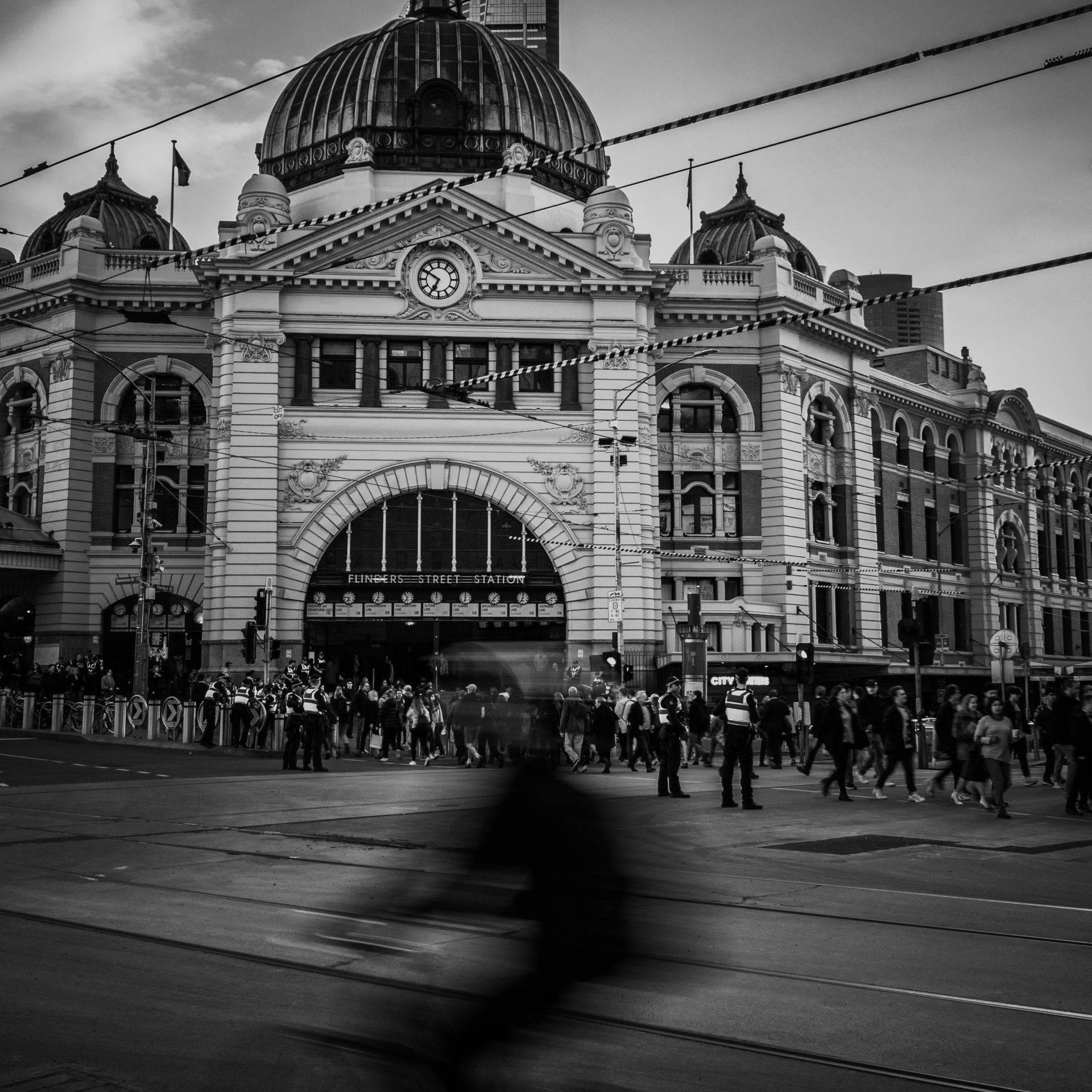 Estação Flinders Street em Melbourne com uma figura desfocada em primeiro plano, movimentada. Preto e branco.