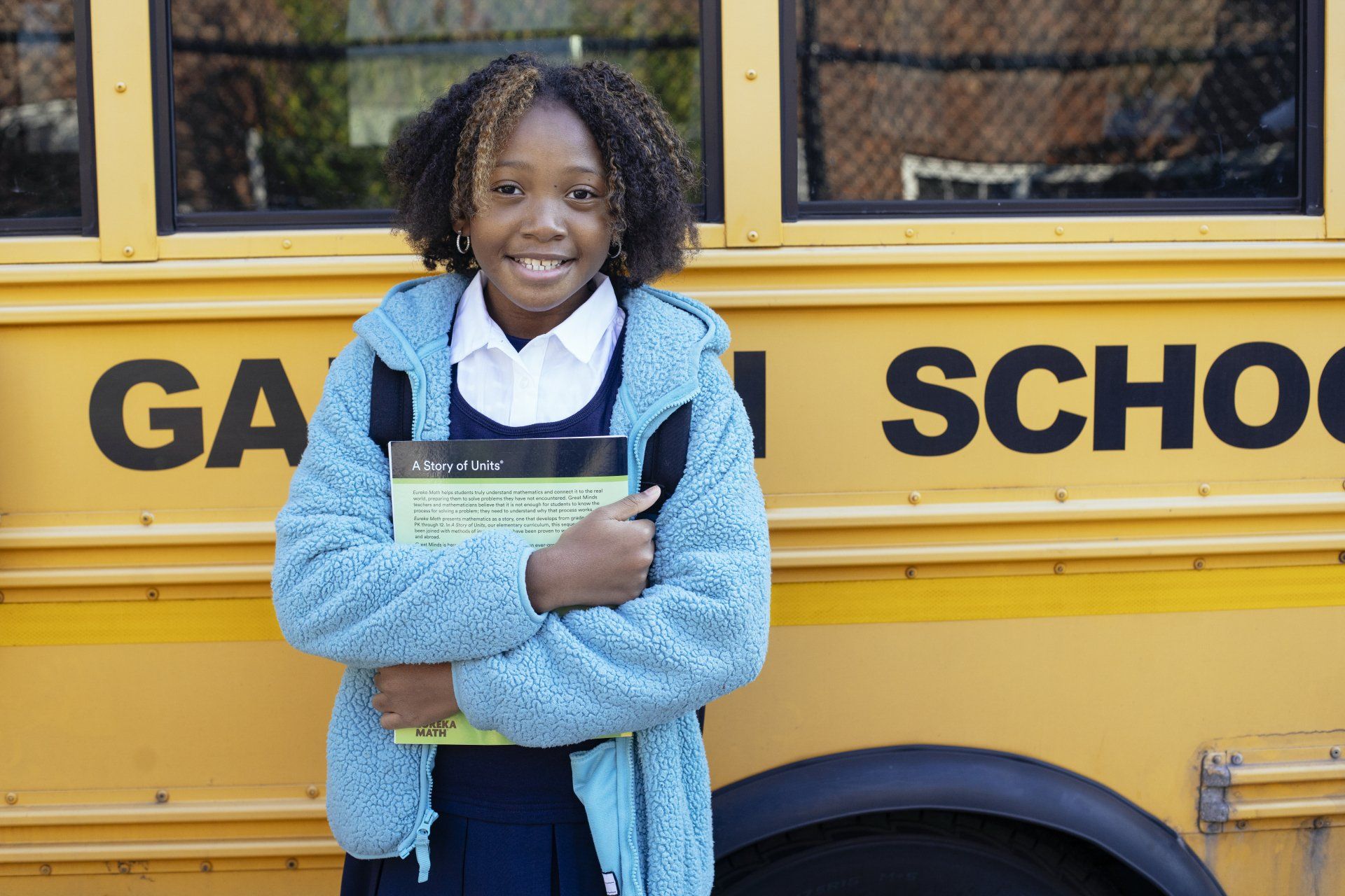 A girl stands in front of a yellow school bus