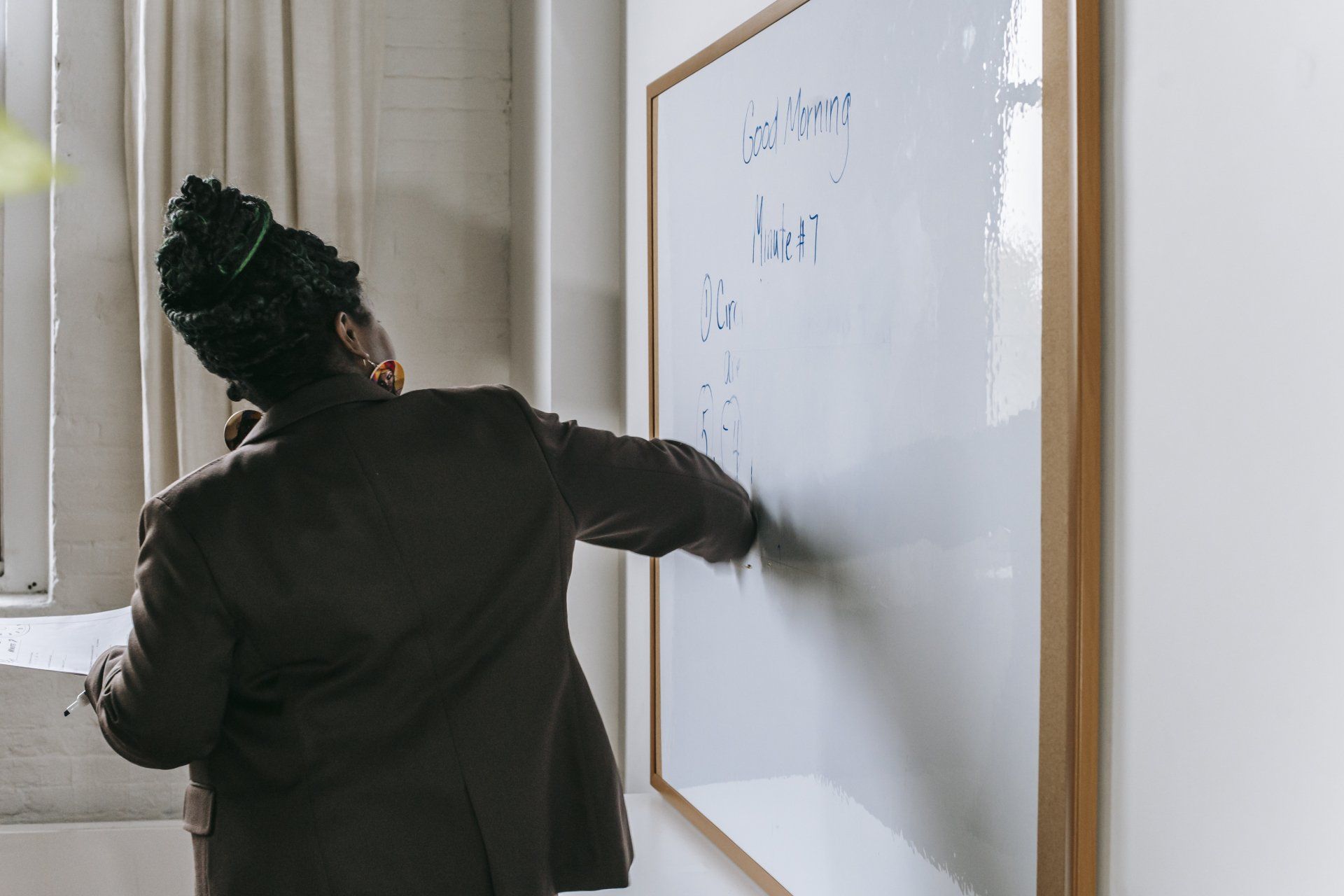 A woman is pointing at a whiteboard in a classroom.