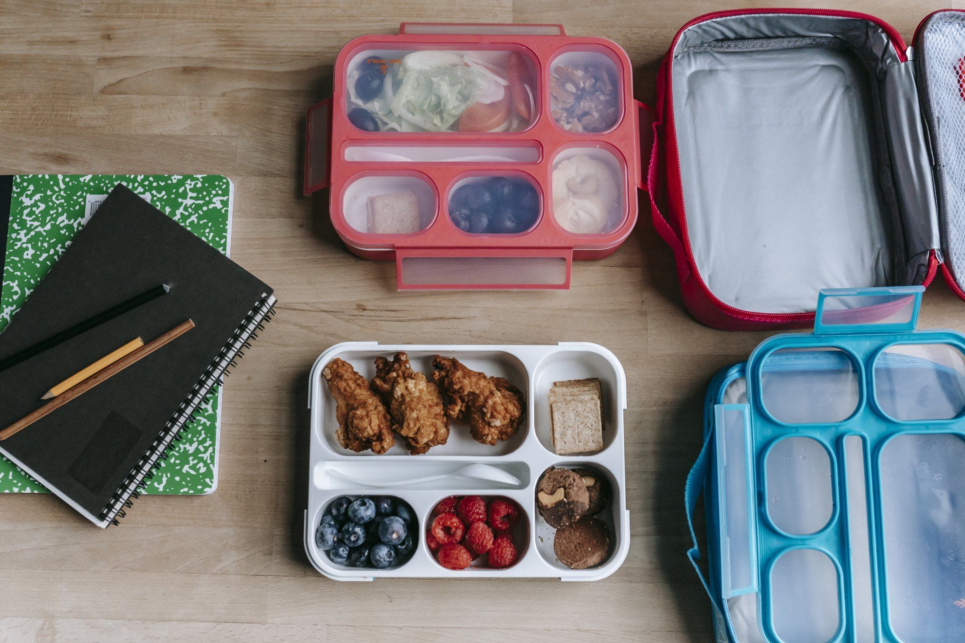 A wooden table topped with lunch boxes and notebooks.