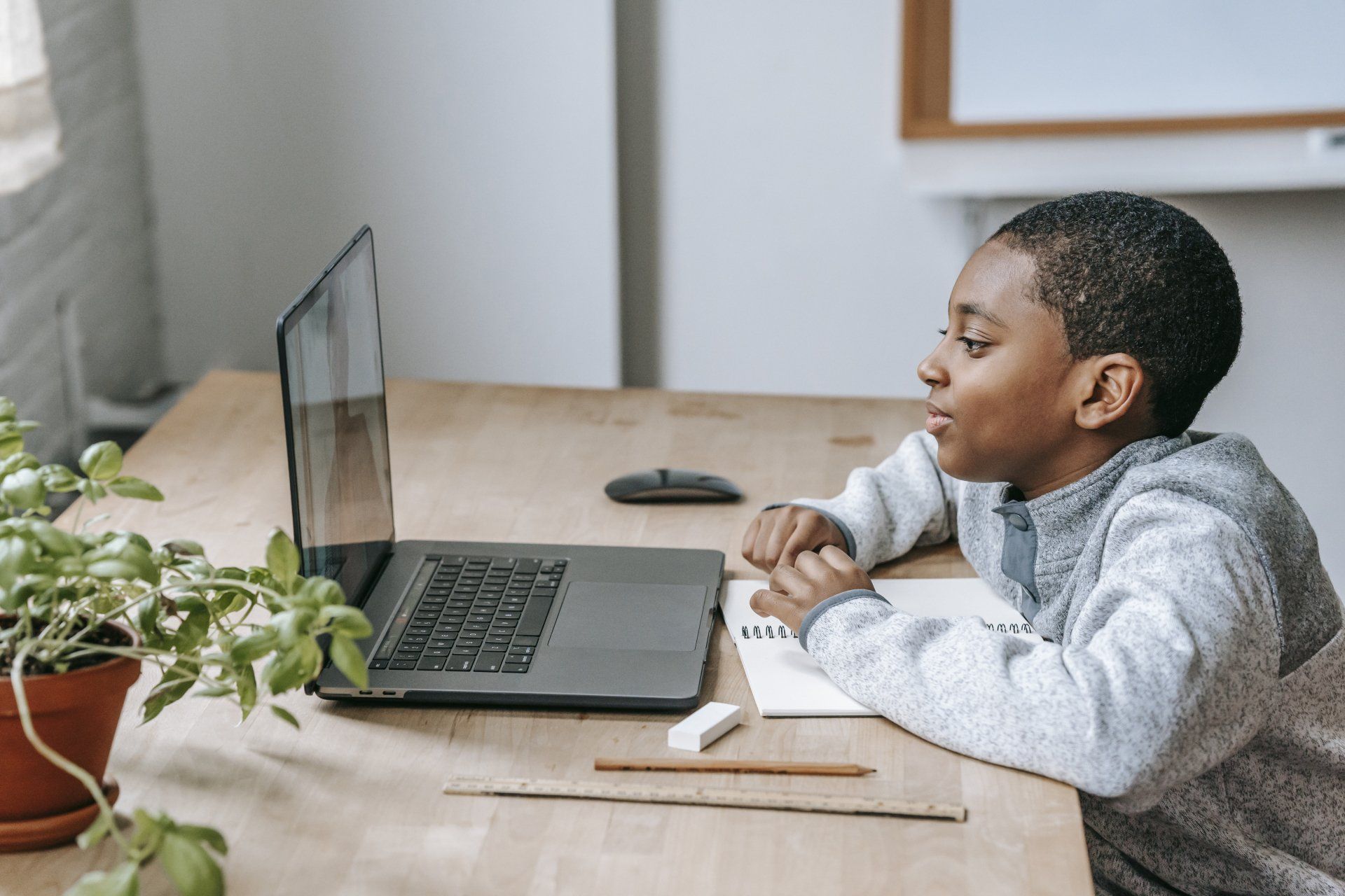 A young boy is sitting at a desk looking at a laptop computer.